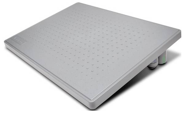 Grå golvmatta med något lutande yta och upphöjningar för bättre grepp. Den vilar på två rullar och är ergonomiskt utformad.