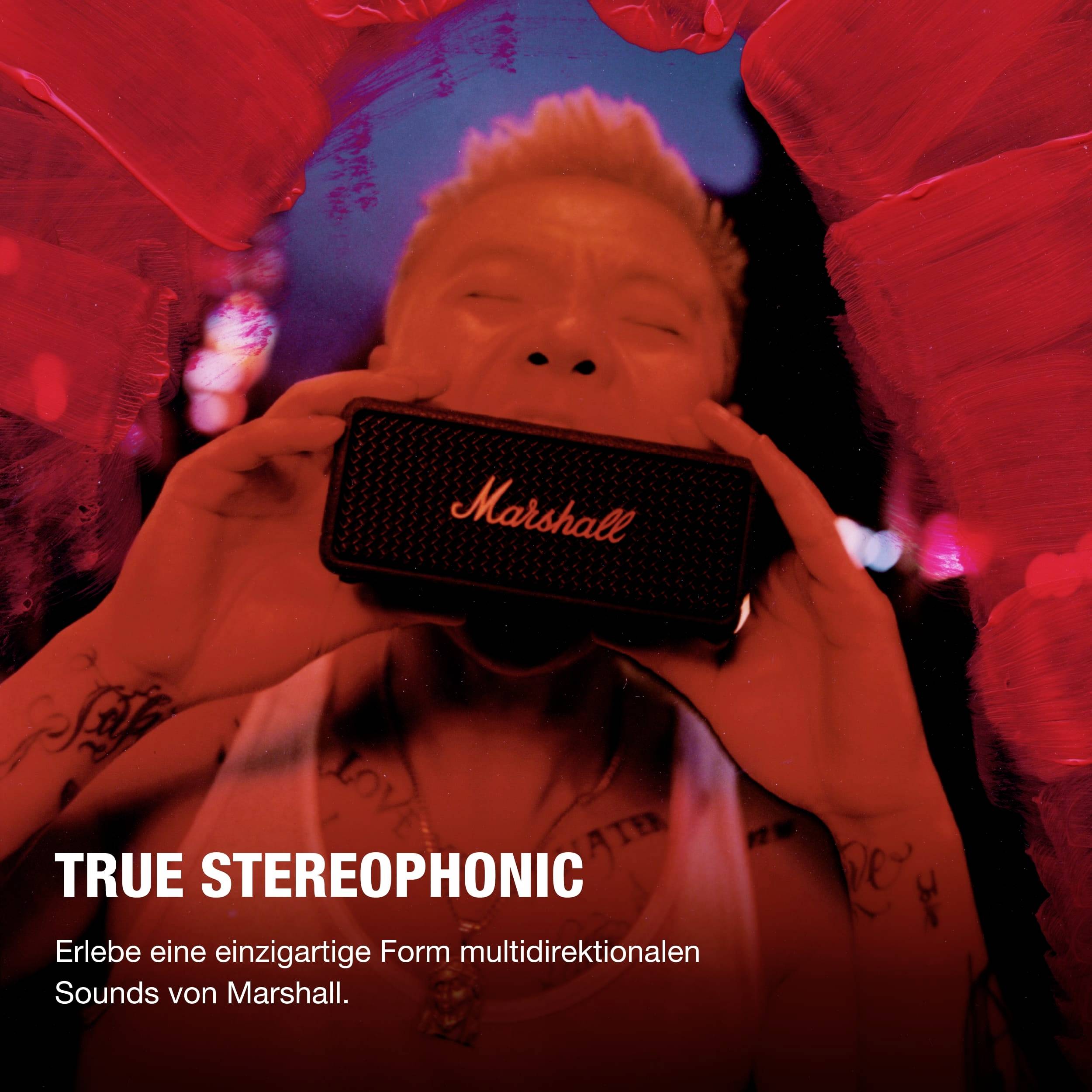 En person håller en svart Marshall-högtalare framför en röd bakgrund. Text: TRUE STEREOPHONIC. Upplev multidirektionellt ljud.