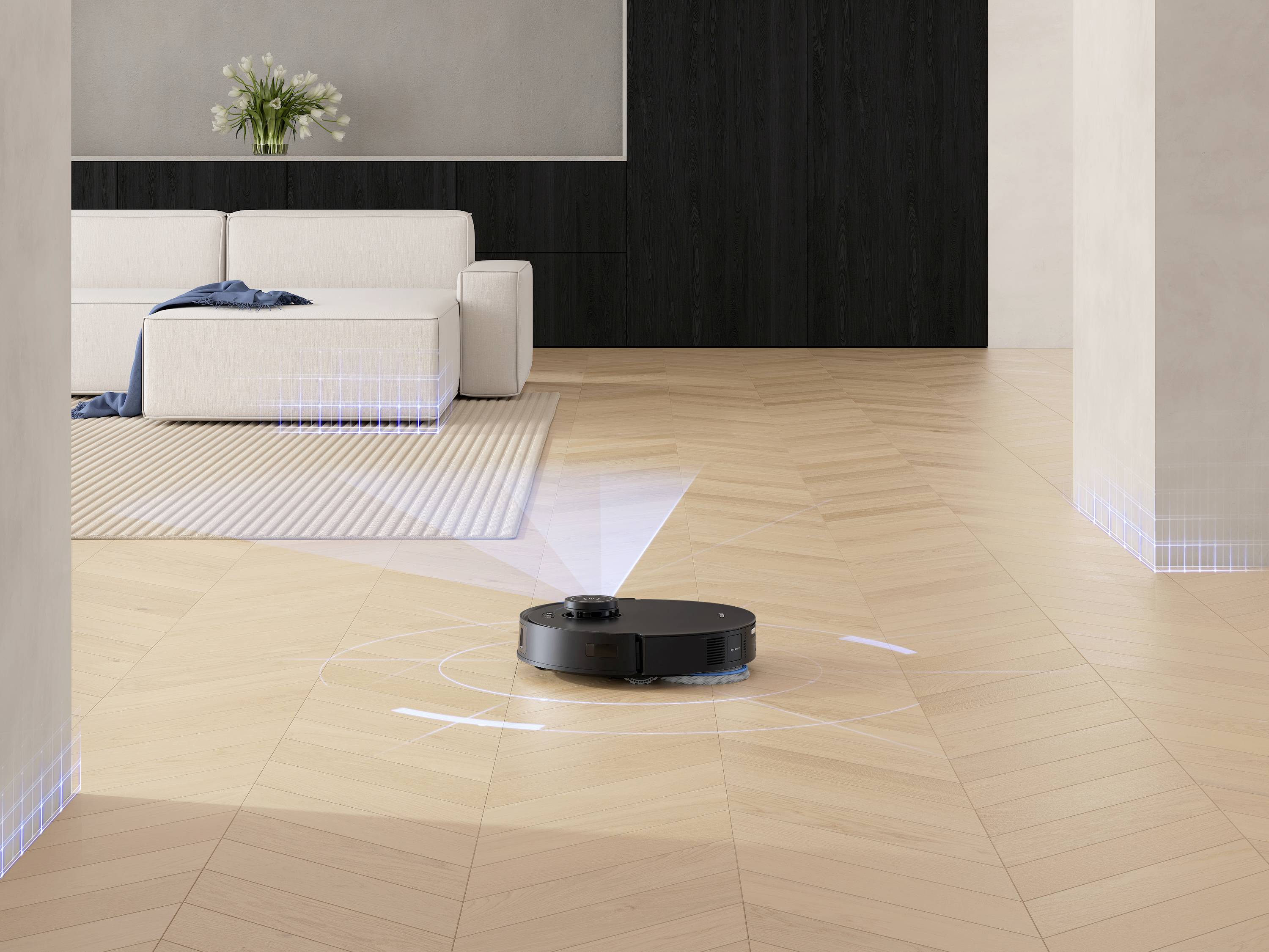 En robotdammsugare rengör trägolvet i ett modernt vardagsrum med en vit soffa, växter och en matta.