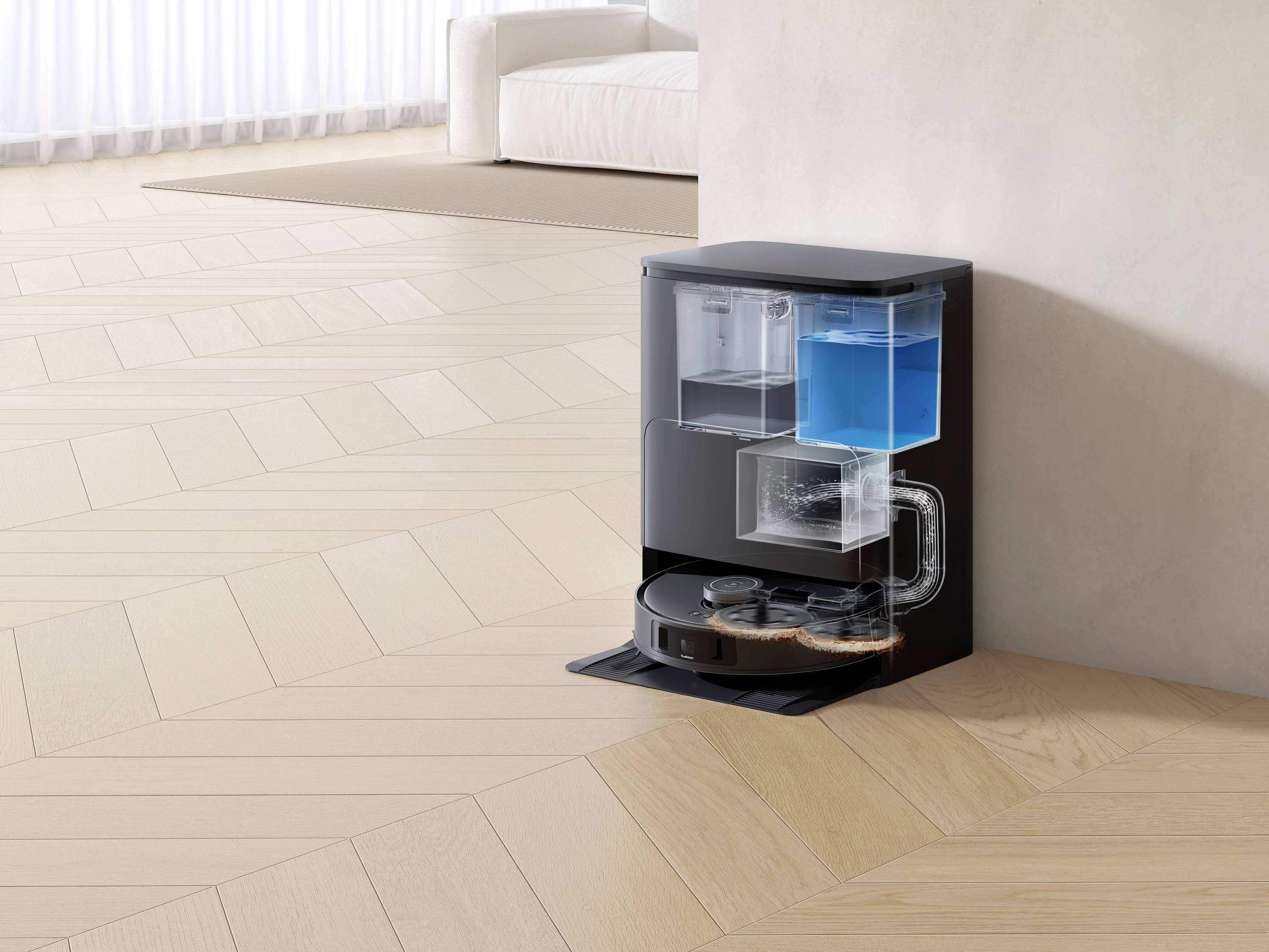 En robotdammsugare i ett hörn tömmer sin behållare i en basstation. Stationen har en blå tank för vätskor.