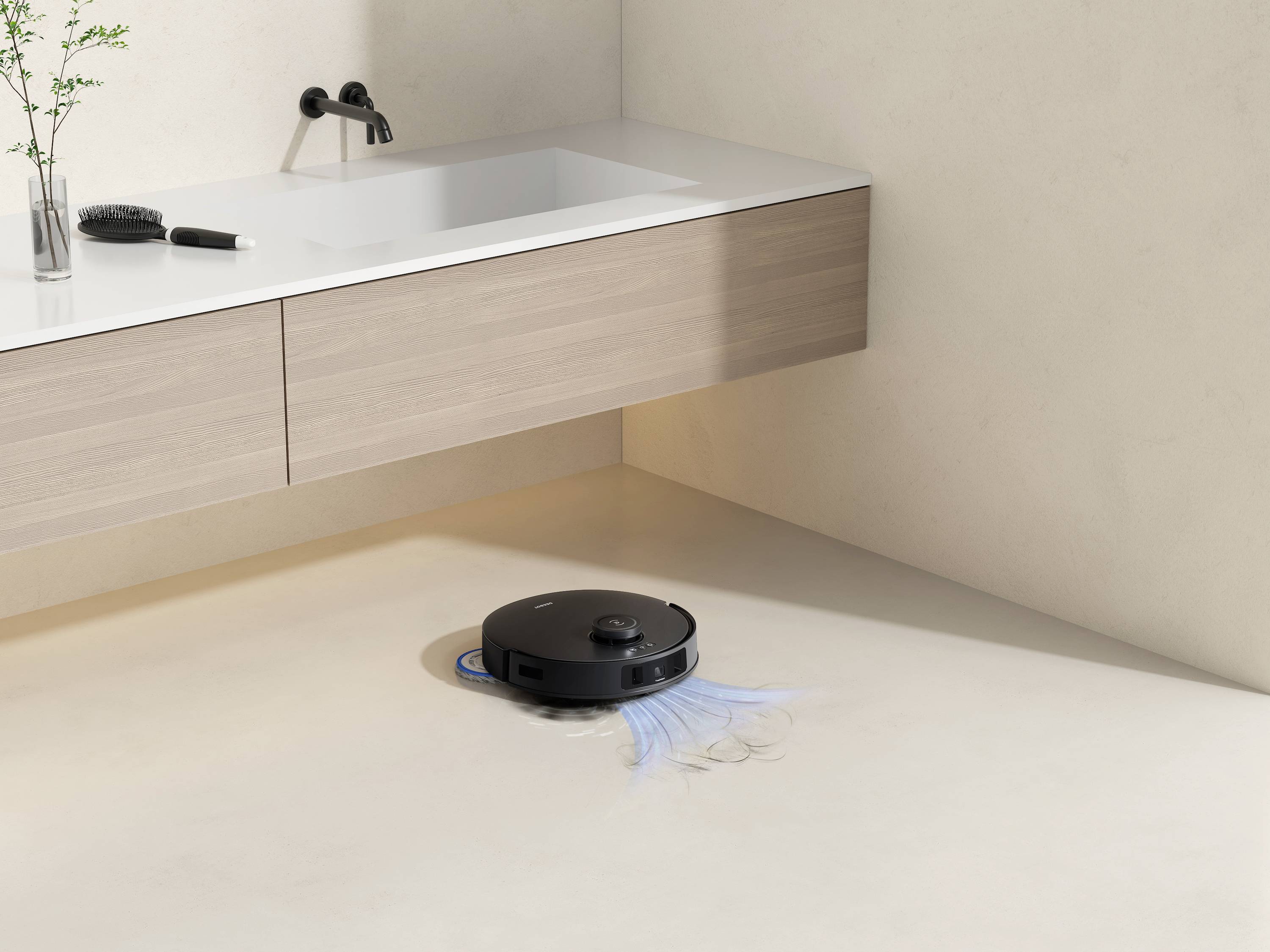 En svart robotdammsugare rengör ett ljust, minimalistiskt designat badrumsgolv. Ett handfat och växter syns.