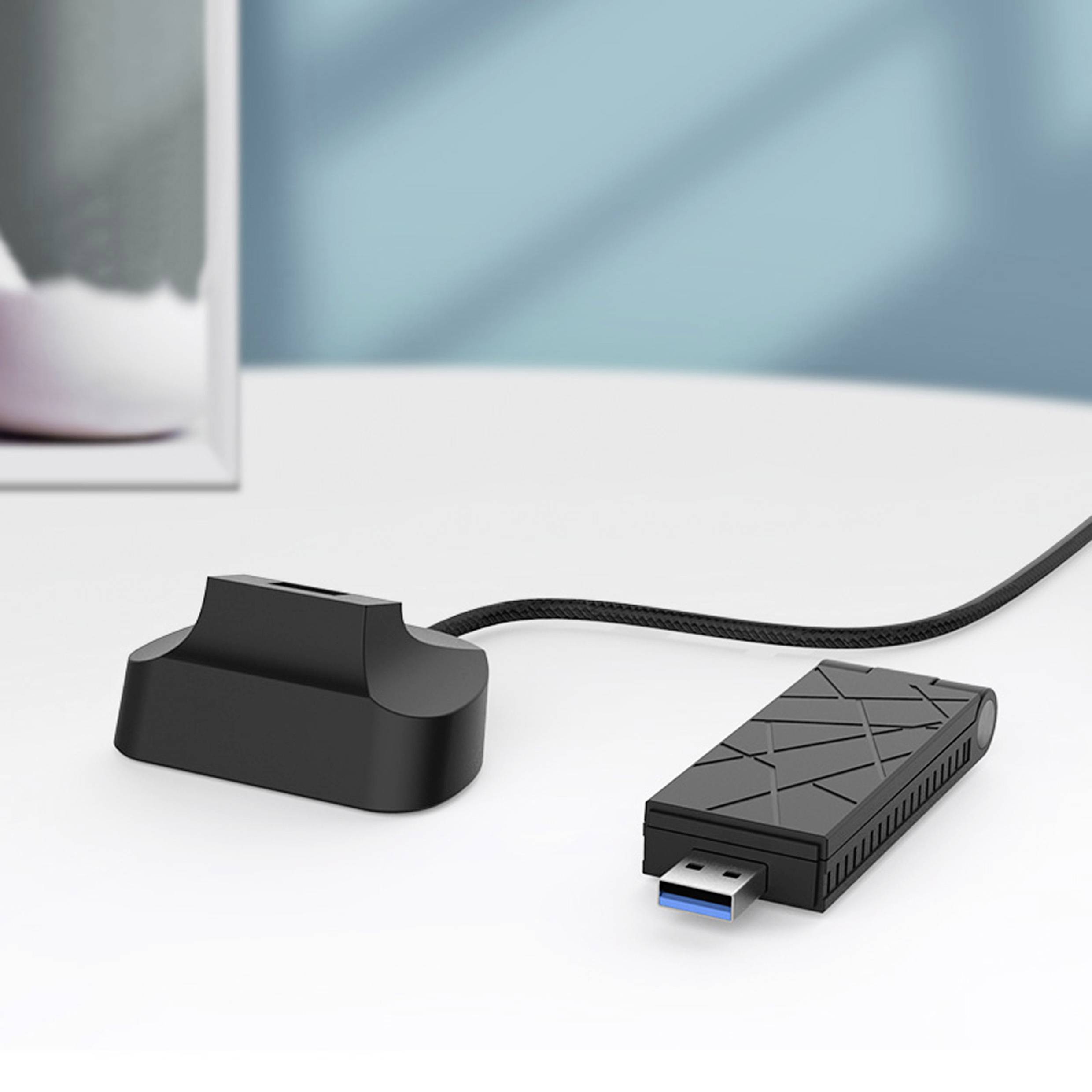 En USB-adapter med strukturerat hölje ligger på en vit yta, ansluten till en liten, svart dockningsstation.