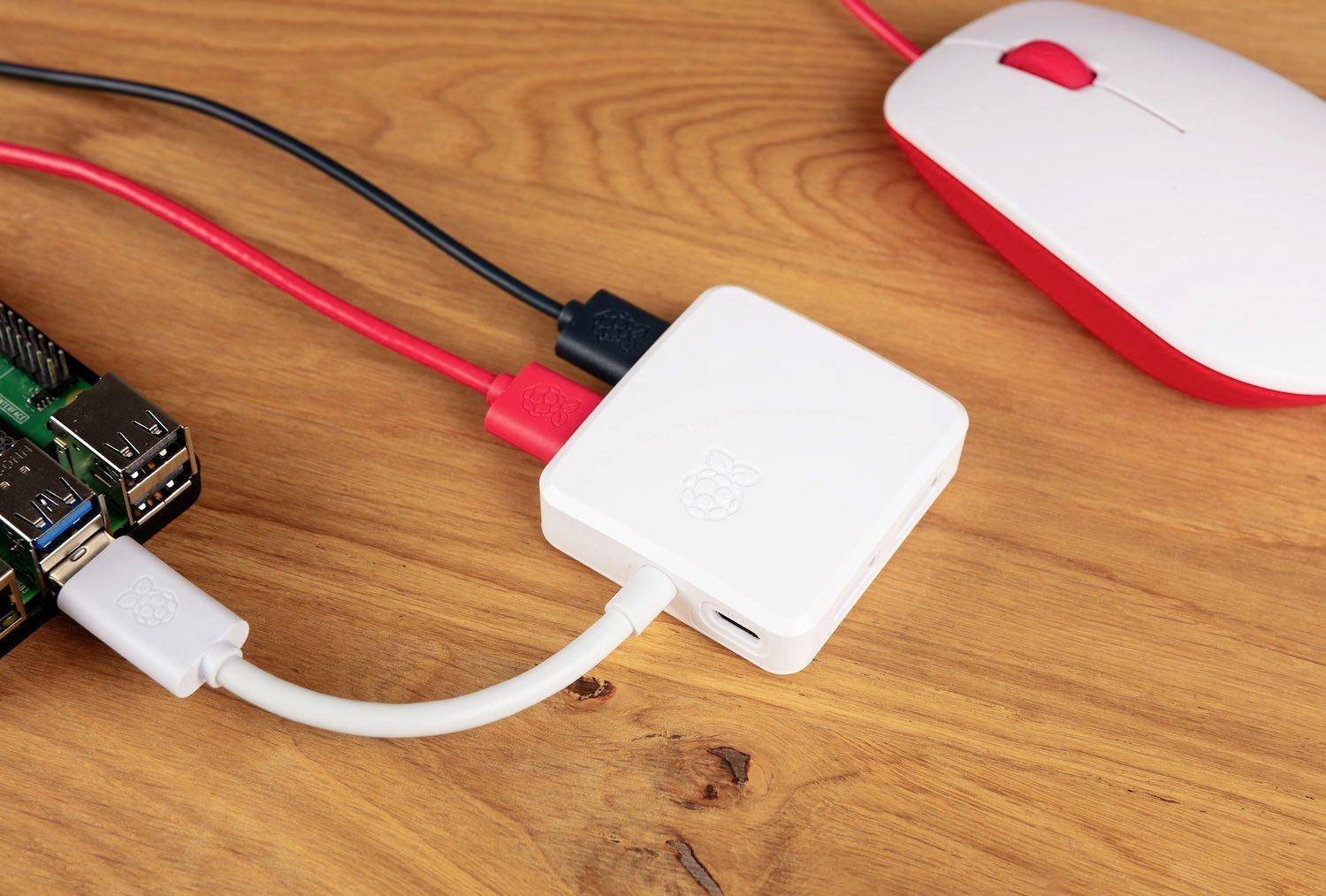 En vit datormus och en USB-hubb är anslutna till en Raspberry Pi som ligger på ett träbord.