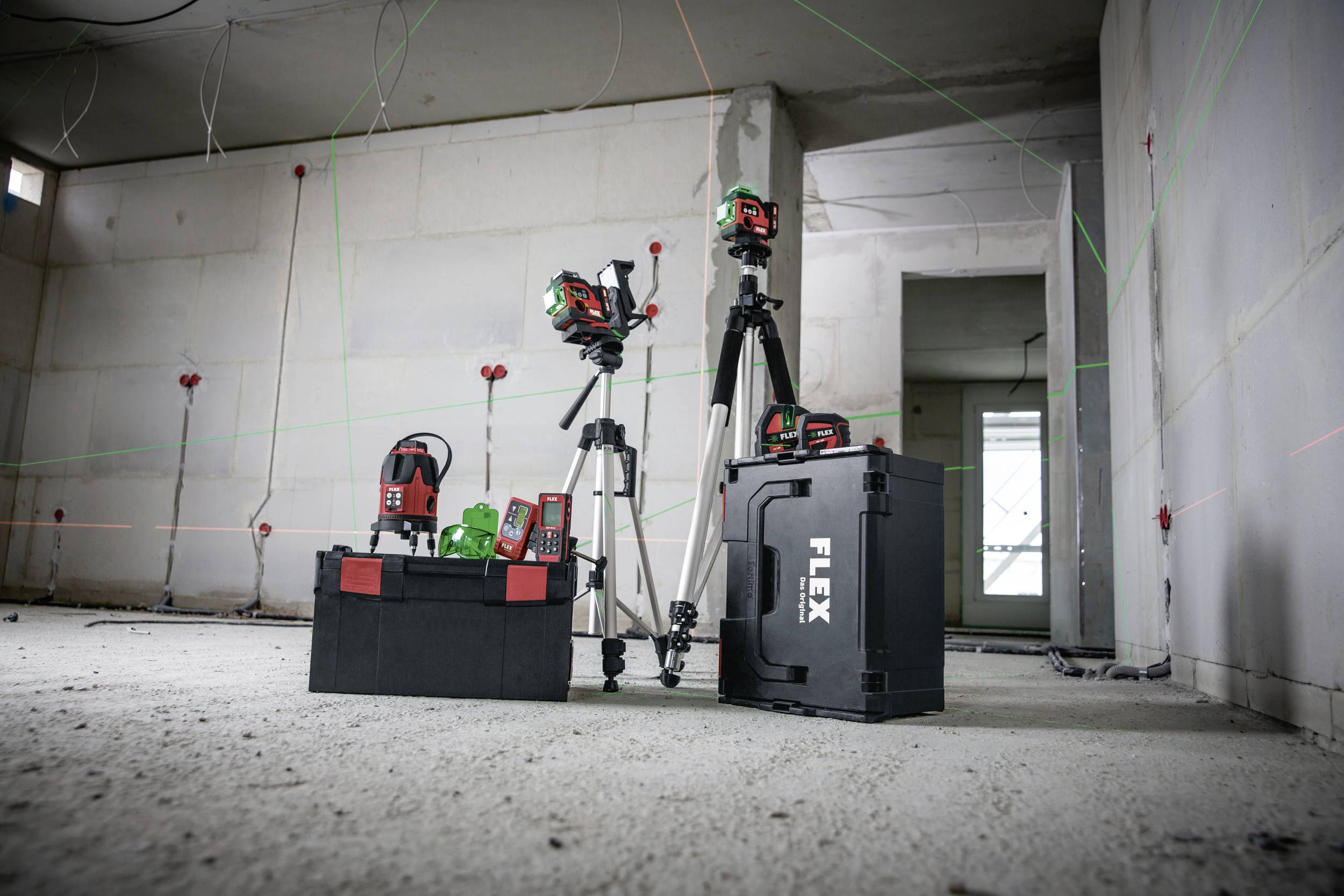 Flera lasermätinstrument och tillbehörsdelar står på ett obearbetat betonggolv i ett ofärdigt rum. Laserlinjer syns på väggarna.