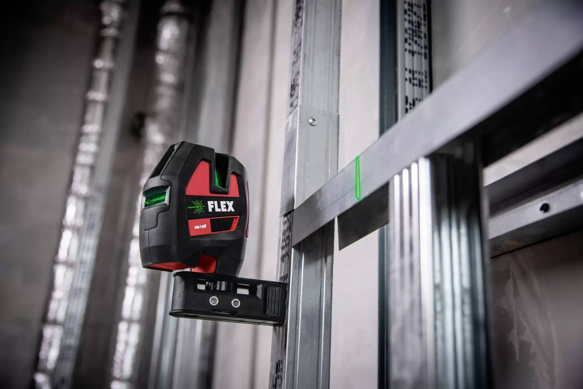 En lasernivåinstrument är fäst vid en metallstruktur och visar gröna linjer på väggen för exakt justering vid byggnadsarbeten.