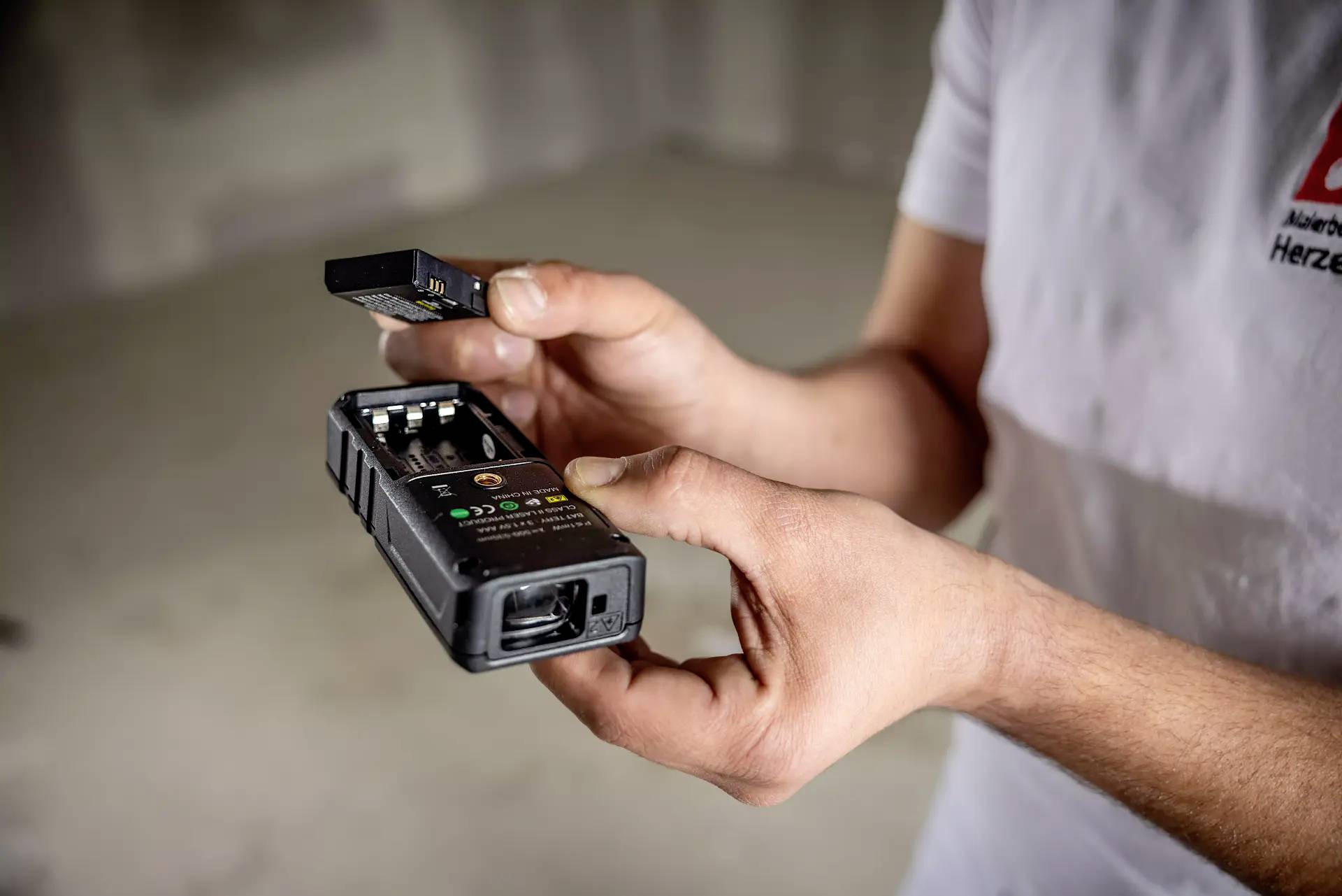 En person håller i ett digitalt multimeter och ett batteri. Personen sätter i batteriet i enheten. Multimetern används för mätningar.
