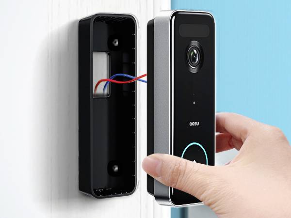 En hand installerar en smart dörrringning med kamera och kablar på en husvägg.