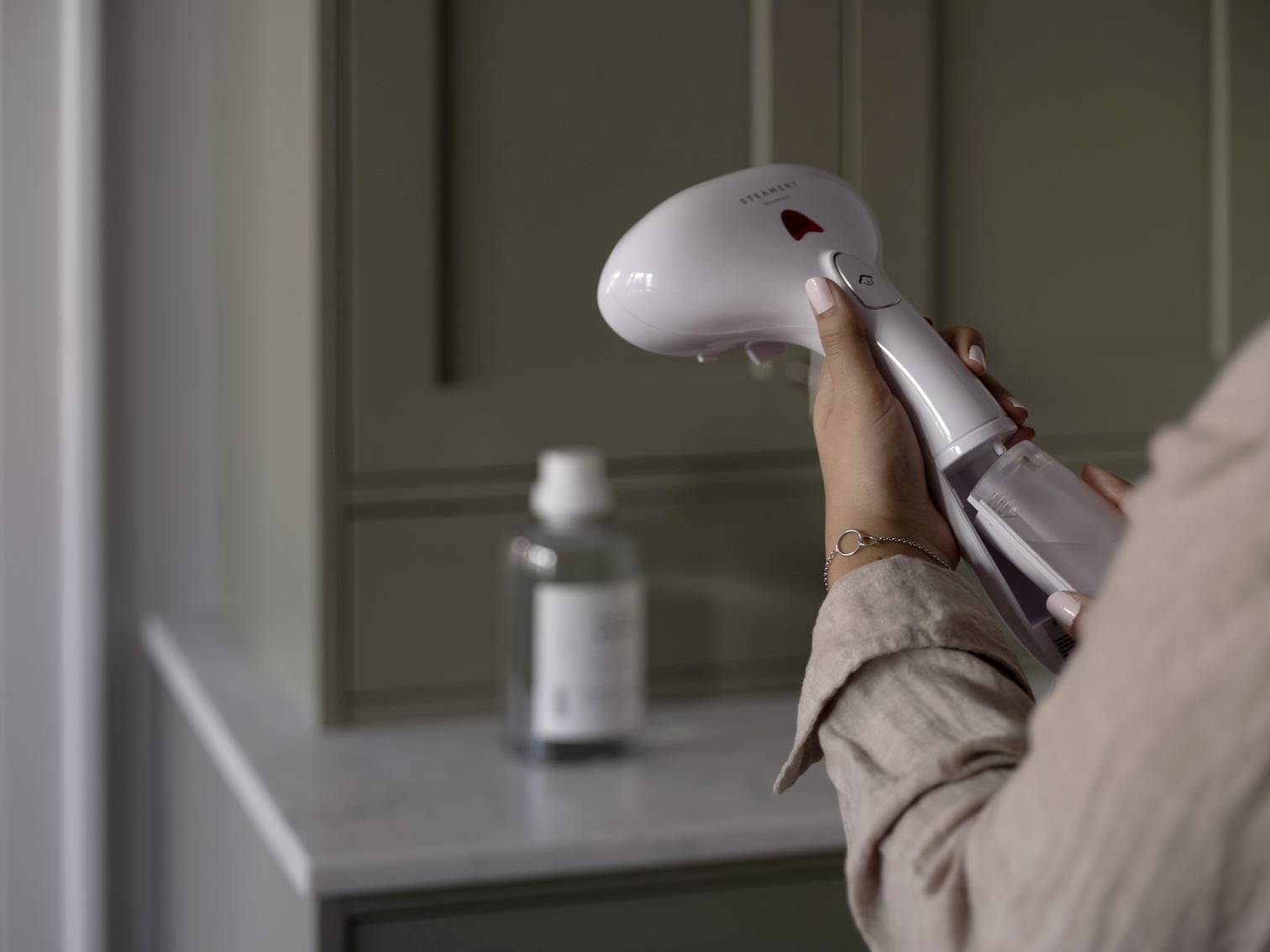 En person håller en handdammare i ett kök eller badrum; i bakgrunden står en flaska på arbetsytan.