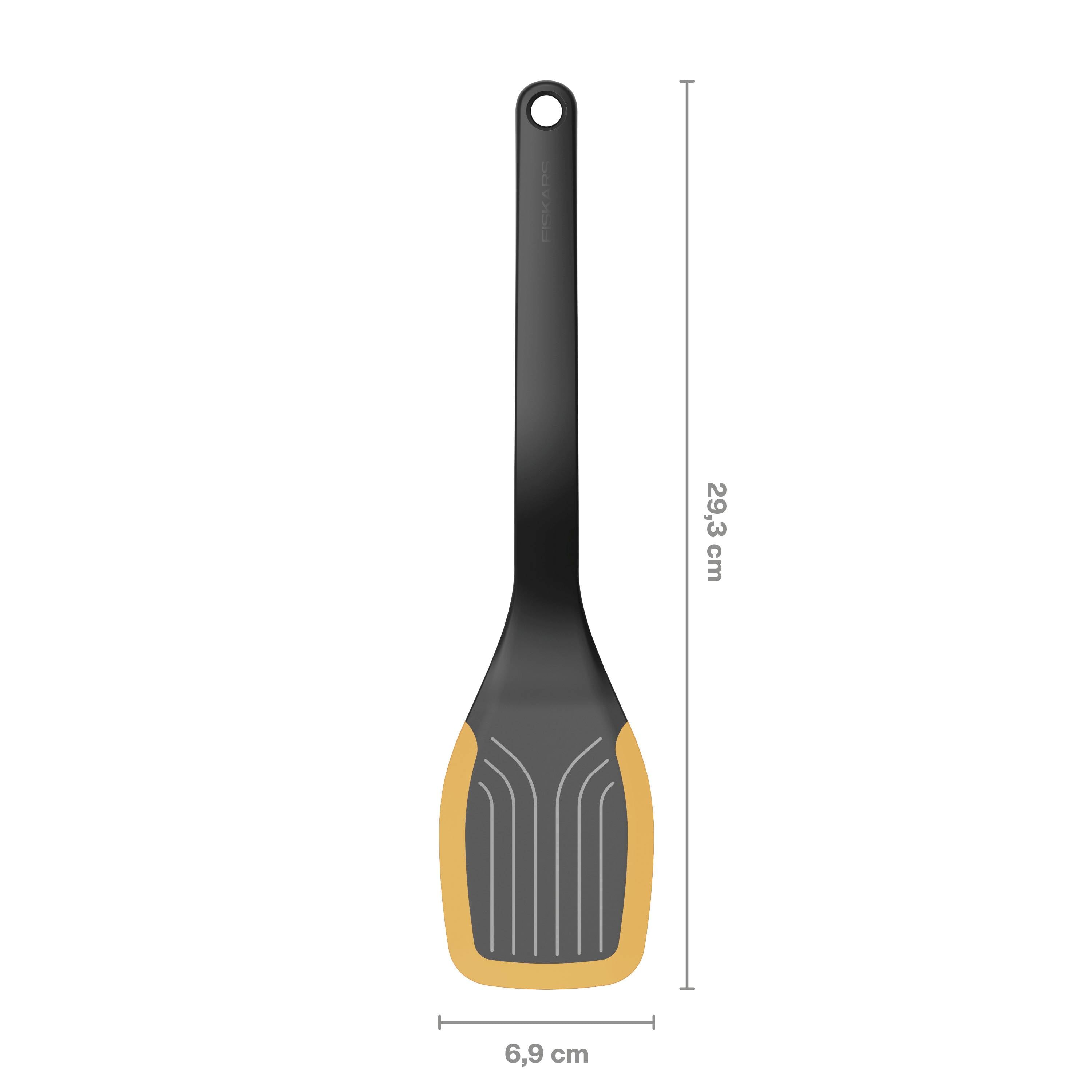 Avbildad är en svart stekspade med orange kant. Längd: 29,3 cm, bredd: 6,9 cm.