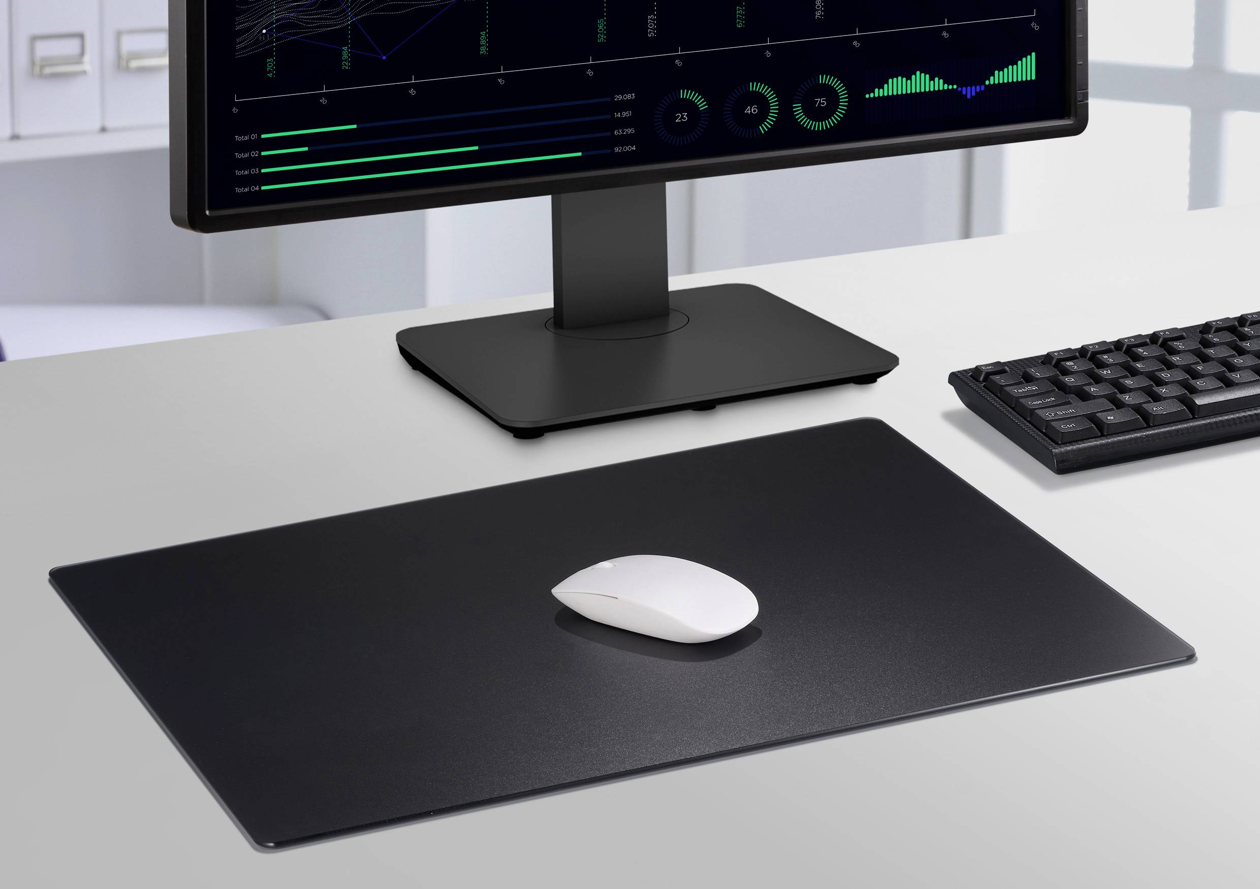 Ett skrivbord med datorskärm, tangentbord och mus på en stor musmatta. Skärmen visar datavisualiseringar.