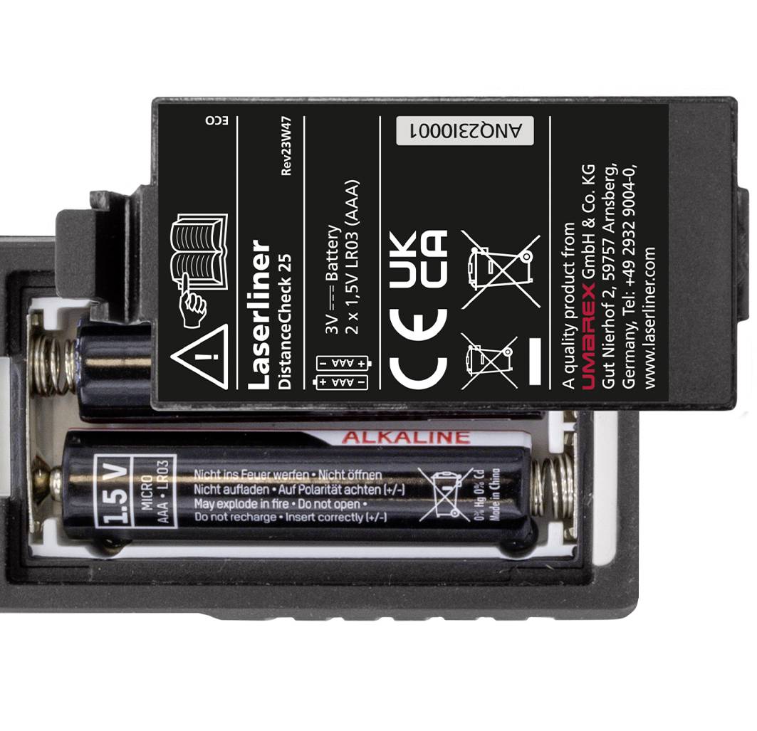 Två AA-alkaliska batterier i ett batterifack, ovanpå en teknisk etikett med tillverkaruppgifter och varningsmeddelanden.