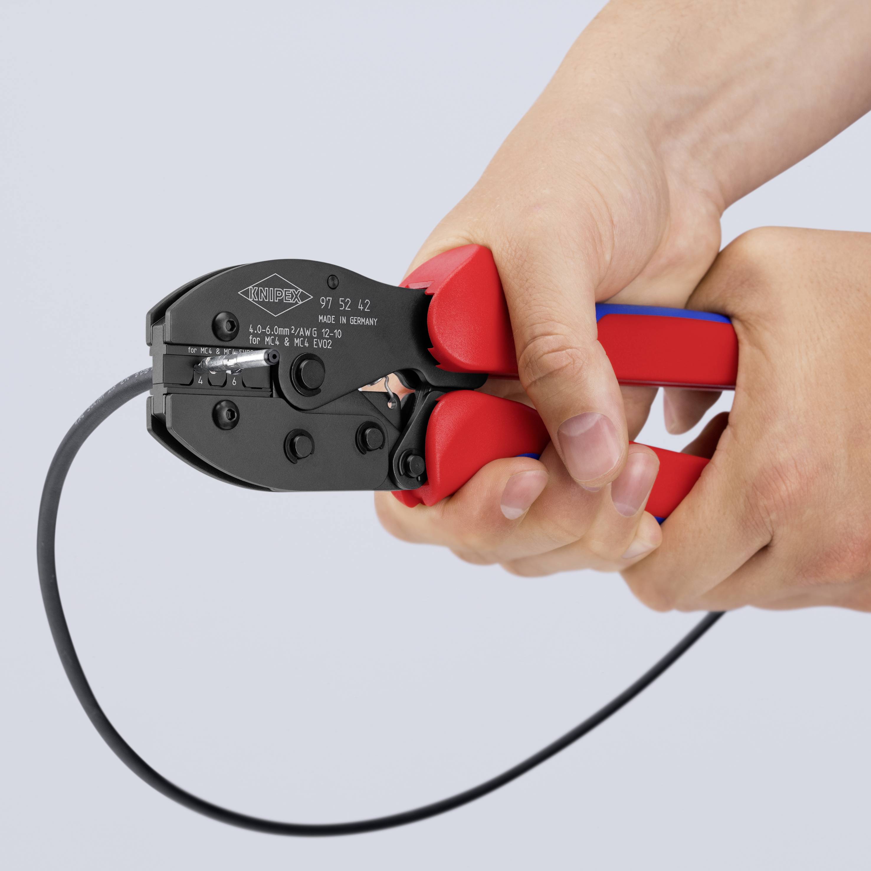 En avbitarतång med röda handtag hålls av en hand medan den klipper en svart kabel.