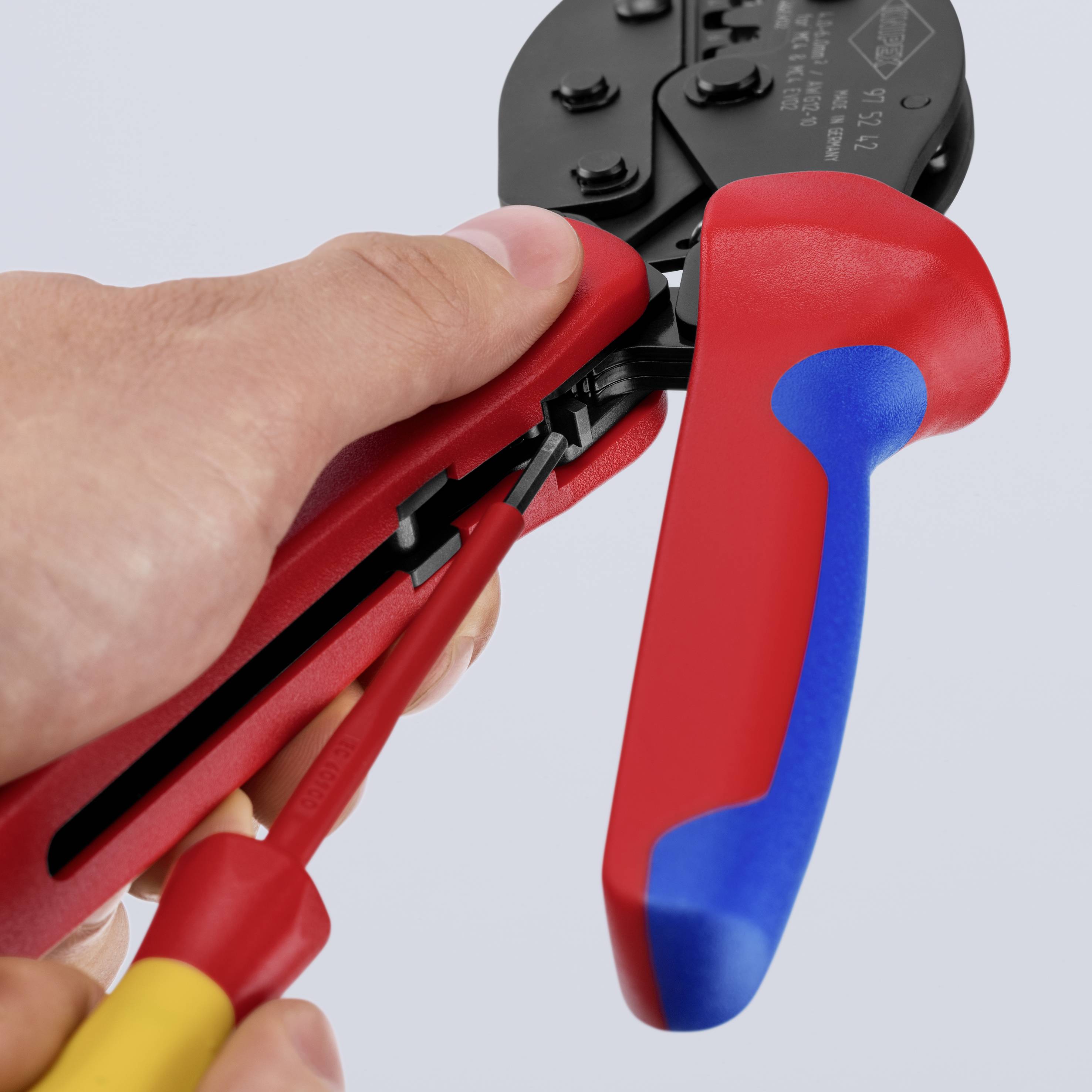 En hand håller en röd crimptång och förbinder en kabel med en kontakt, där precision och hantering står i fokus.