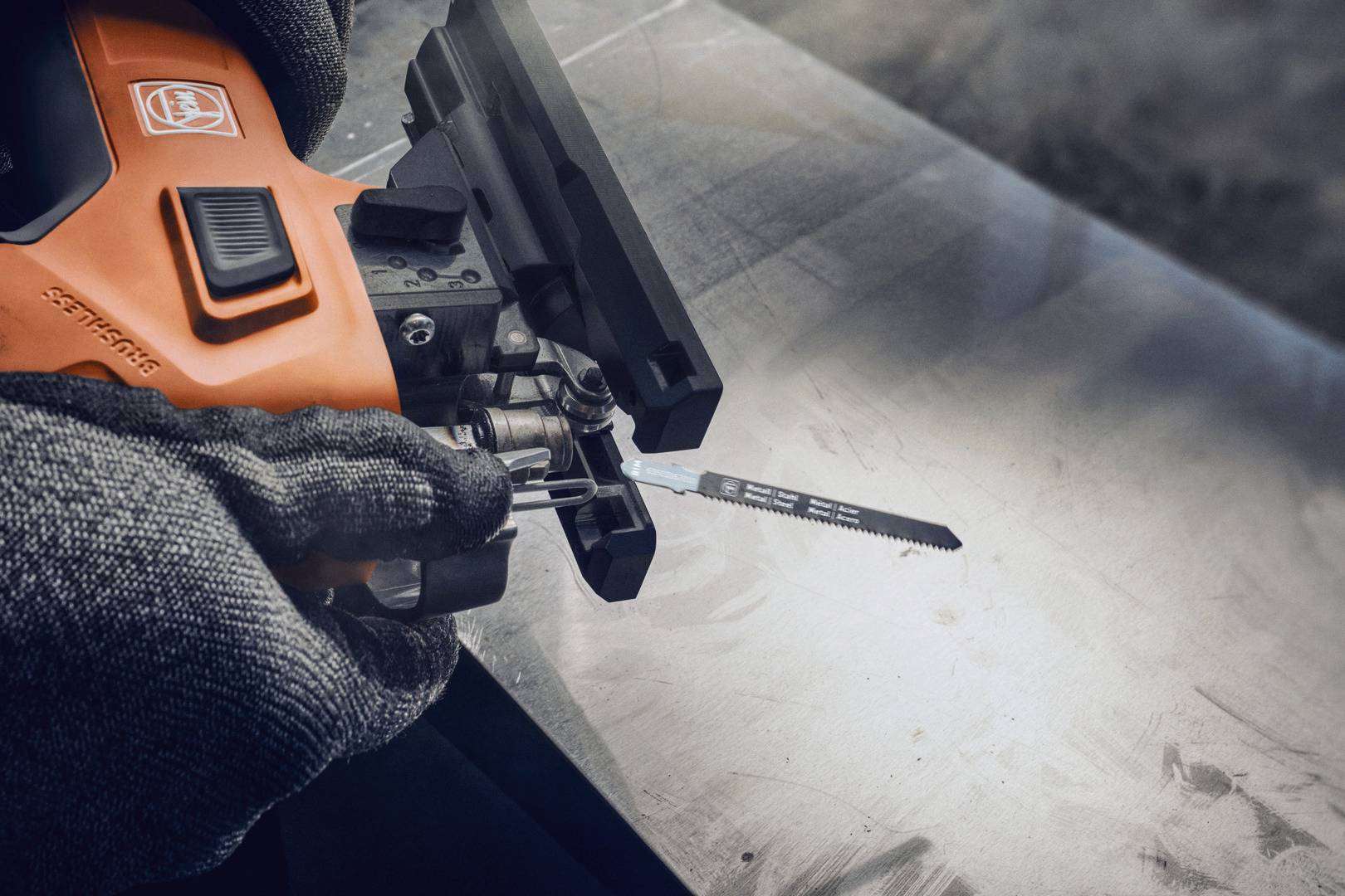 En person i handskar håller en orange elektrisk såg riktad mot en metallbit, förberedd för att såga.