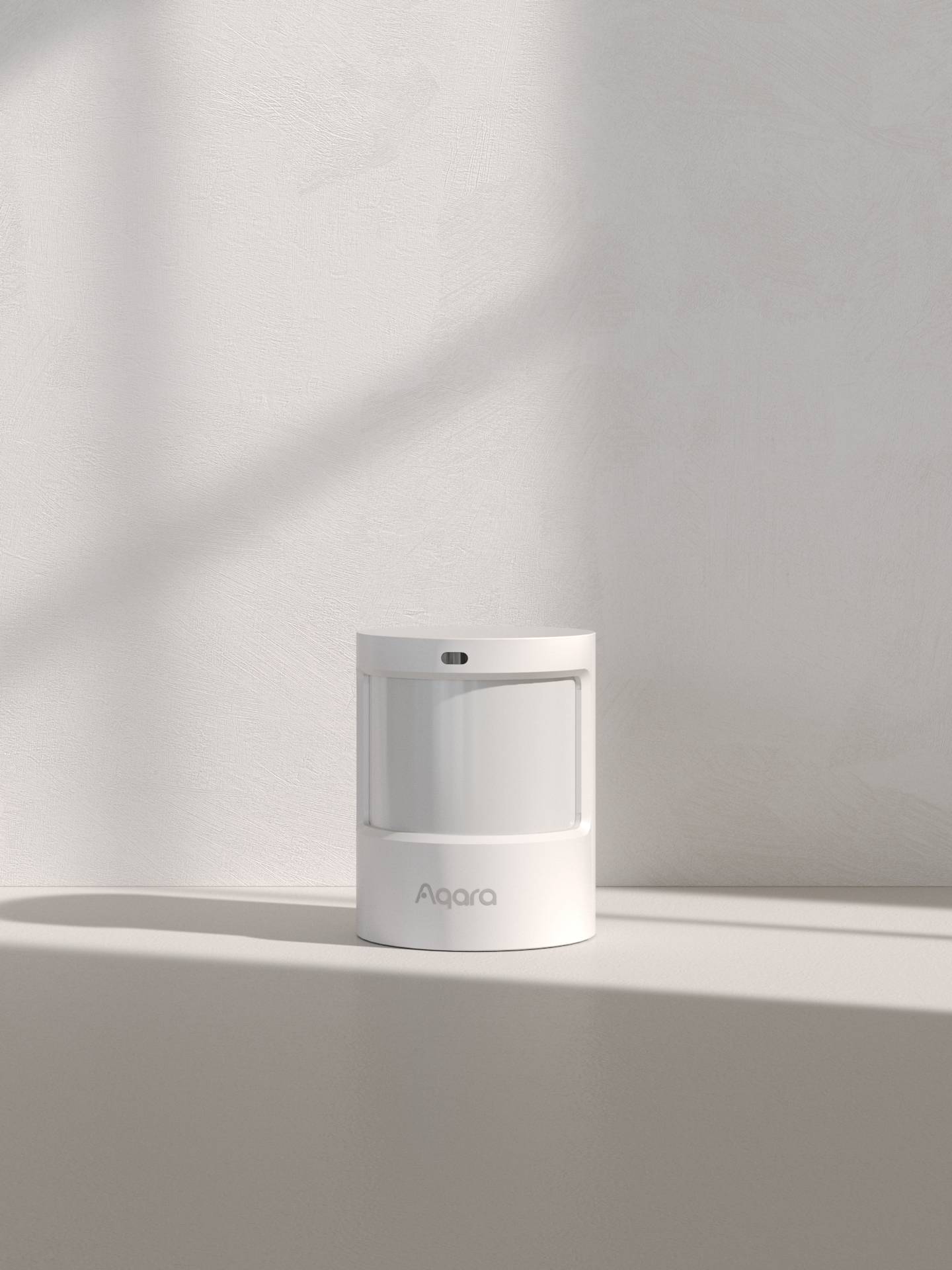 En vit rörelsesensor står på en yta med mjuk skuggbildning. Varumärkesetiketten 'Aqara' är synlig.