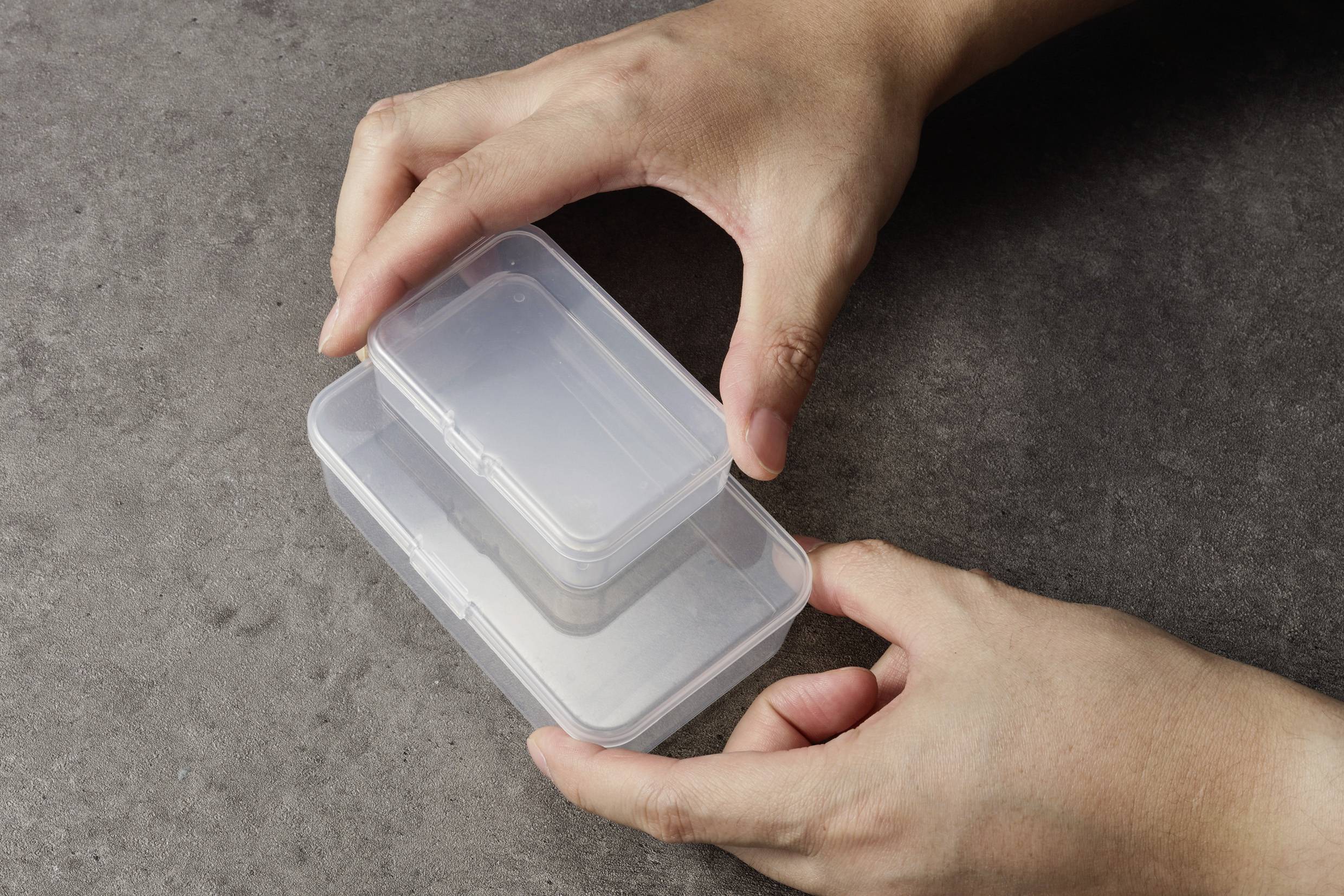 Där stod två transparenta, rektangulära plastbehållare staplade på en grå yta.