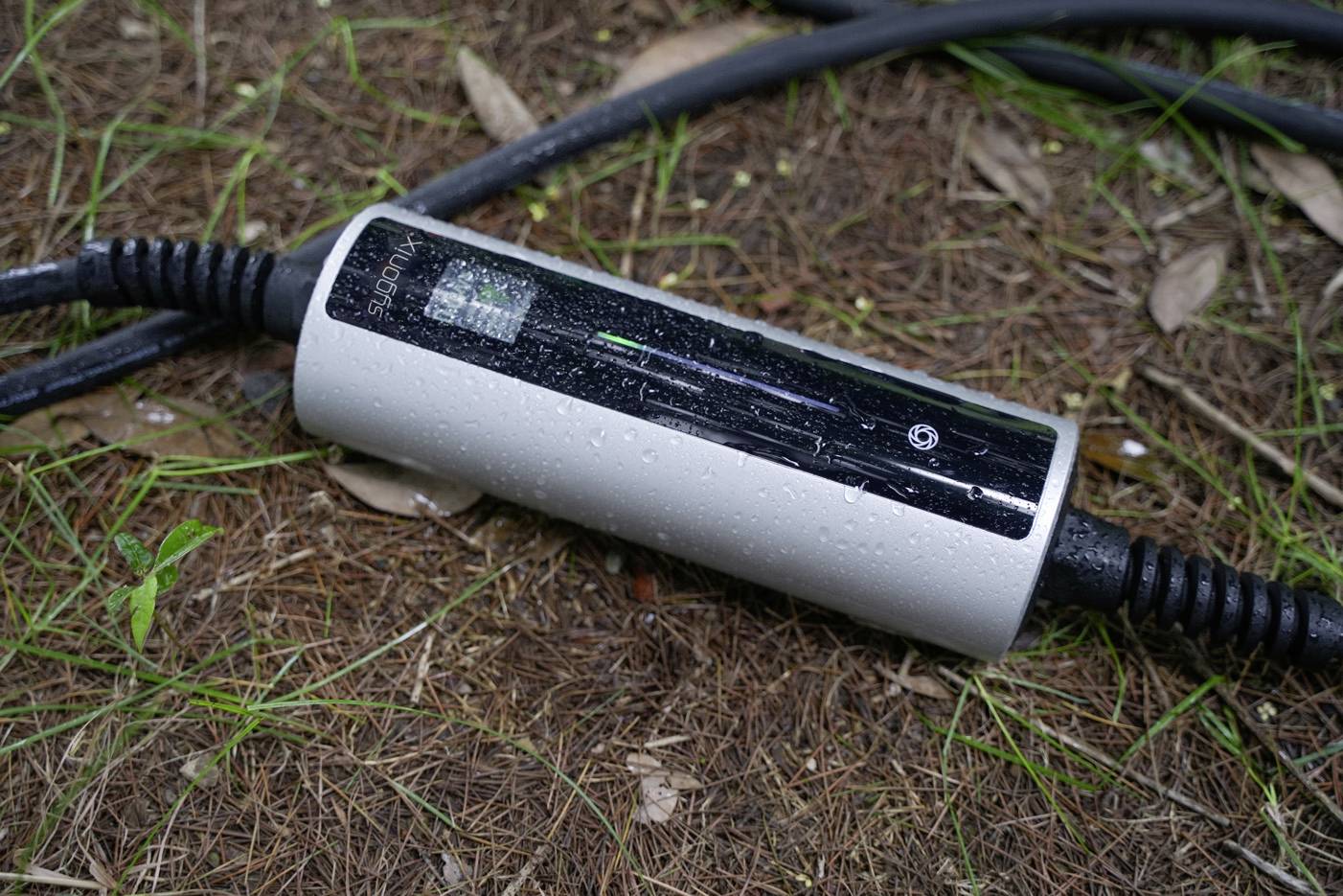 En elektrisk laddkabel ligger på marken utomhus, visad med en AC-laddare som är ansluten till en svart kabel.