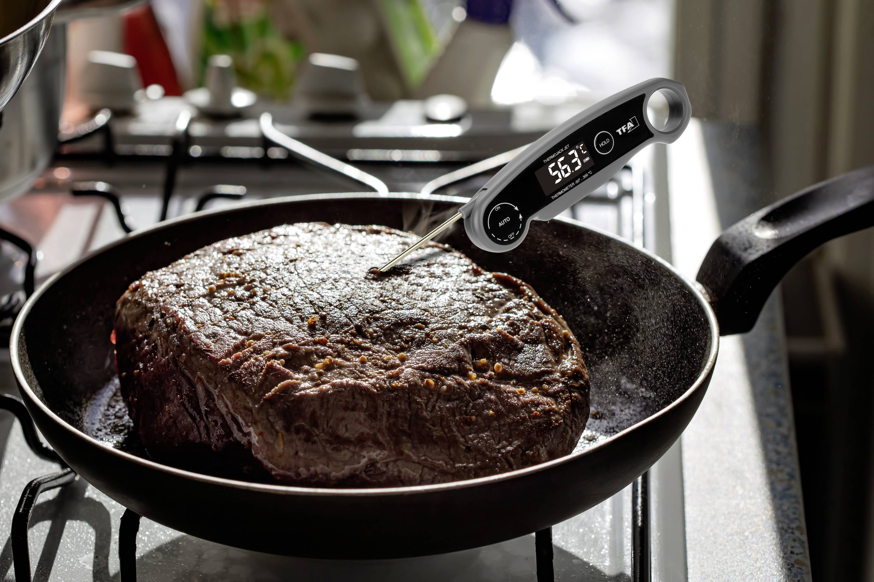 Ett stort stycke kött i en stekpanna mäts med en digital termometer som visar 56,3°C.