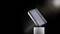 En svart, bärbar powerbank svävar lätt lutad över en cylinderformad sockel framför en svart bakgrund.