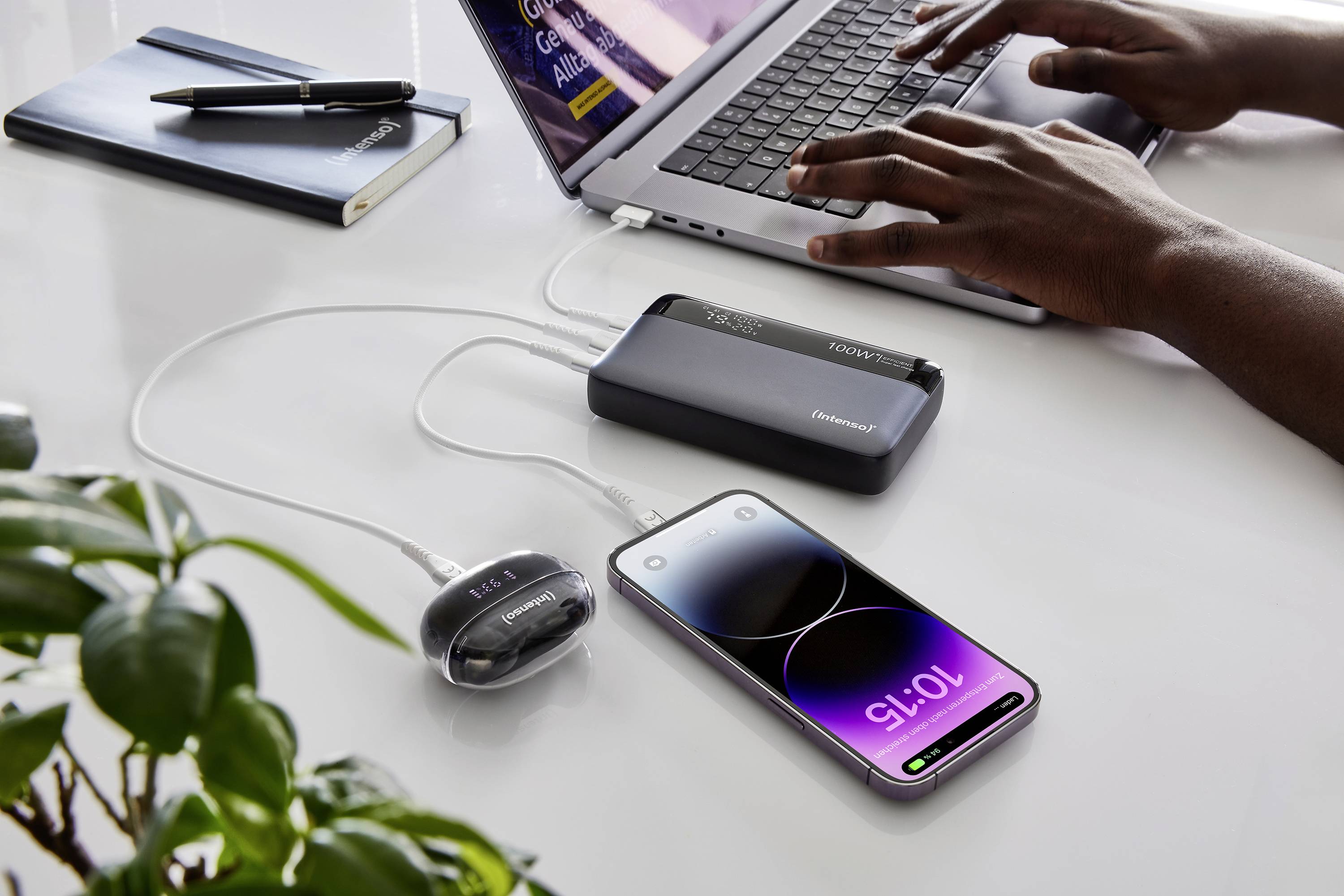 En person arbetar på en bärbar dator medan en smartphone och en annan enhet laddas via en powerbank.