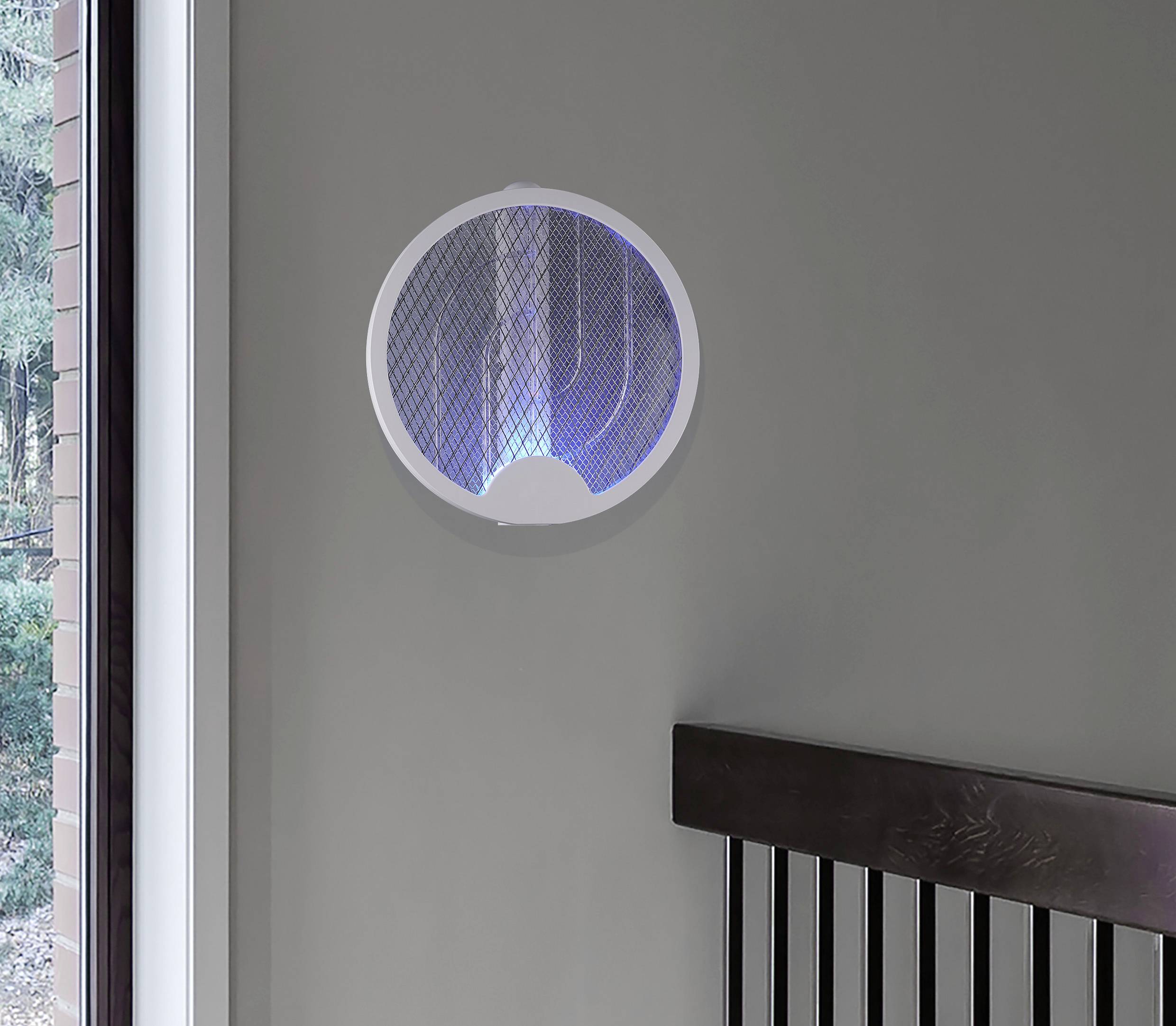 En rund, modern lampa med blått ljus hänger på en grå vägg. Till vänster finns ett fönster med utsikt över grönskan.