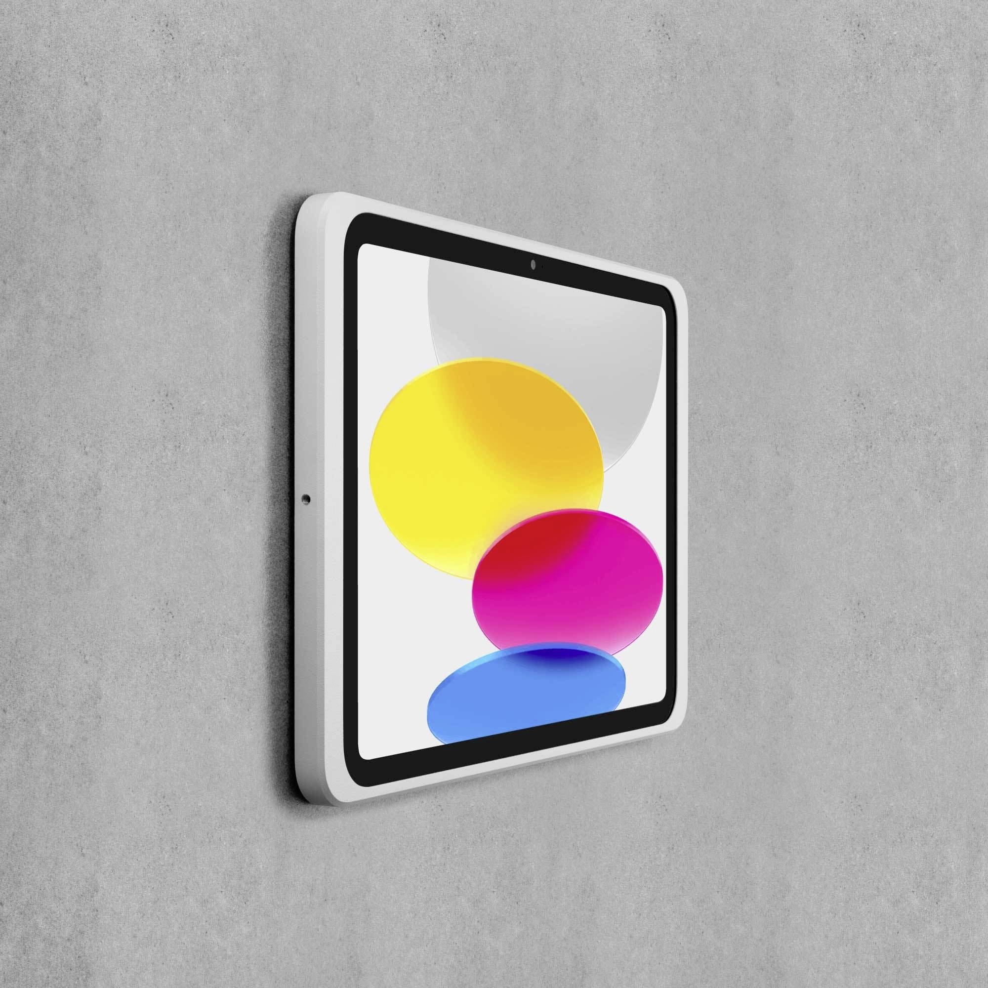 En vit ram med en skärm visar färgrika former: gul, rosa och blå, framför en grå vägg.