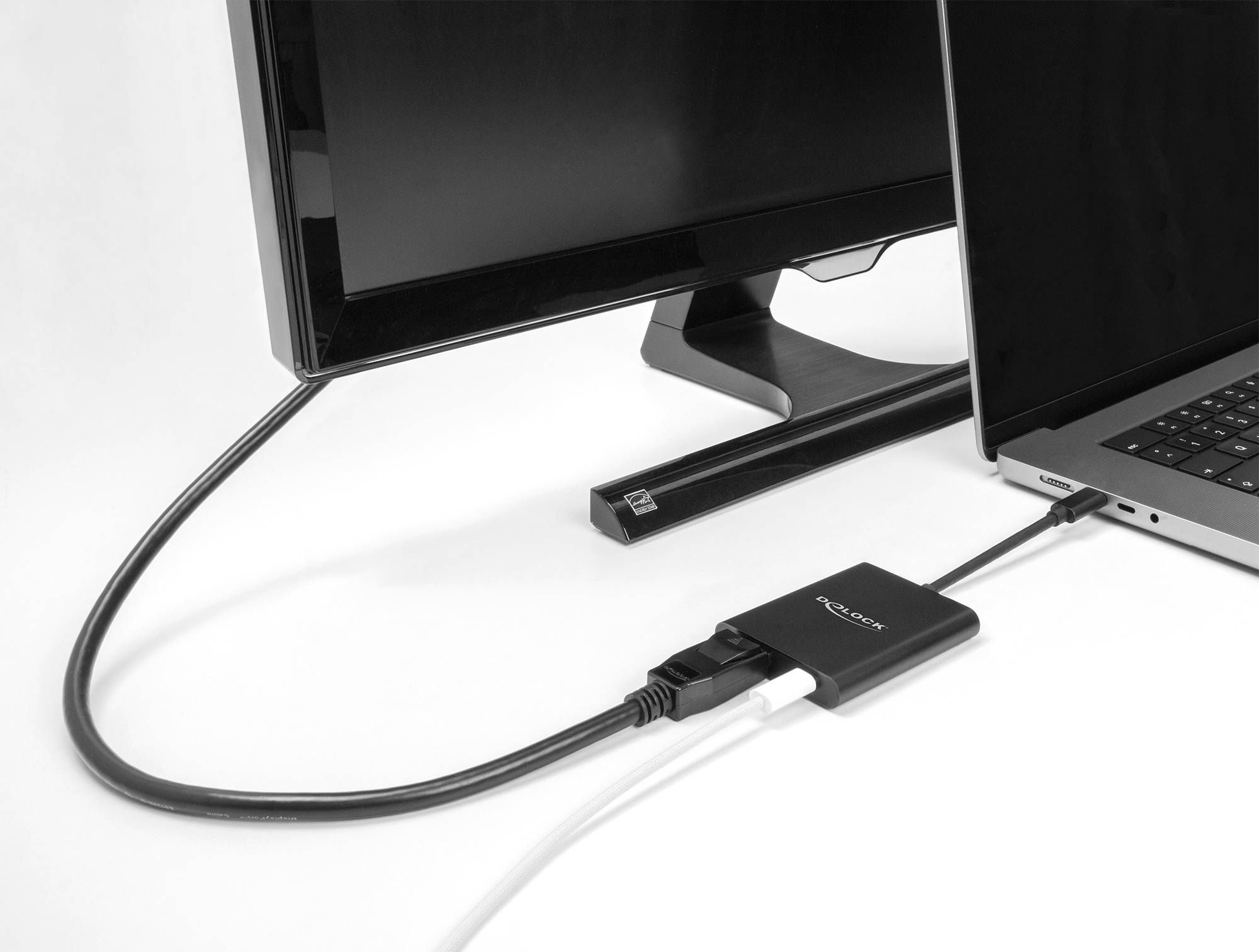 Bärbar dator, ansluten till en bildskärm via ett HDMI-kabel och adapter, mot en vit bakgrund. Huvudtema: Tekniksammankoppling.