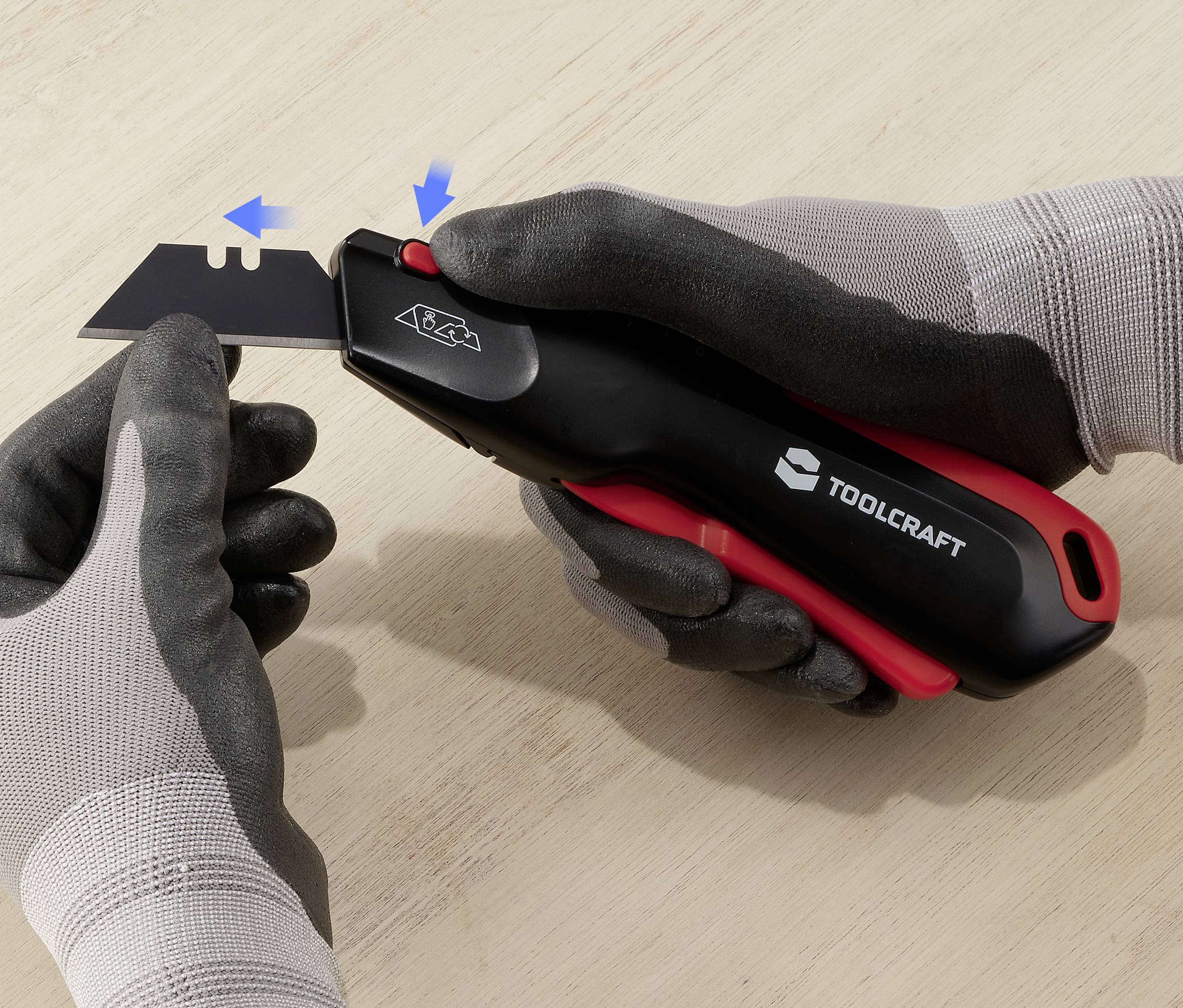 En person med grå handskar byter bladet på en svart skärkniv från Toolcraft genom att aktivera en säkring.