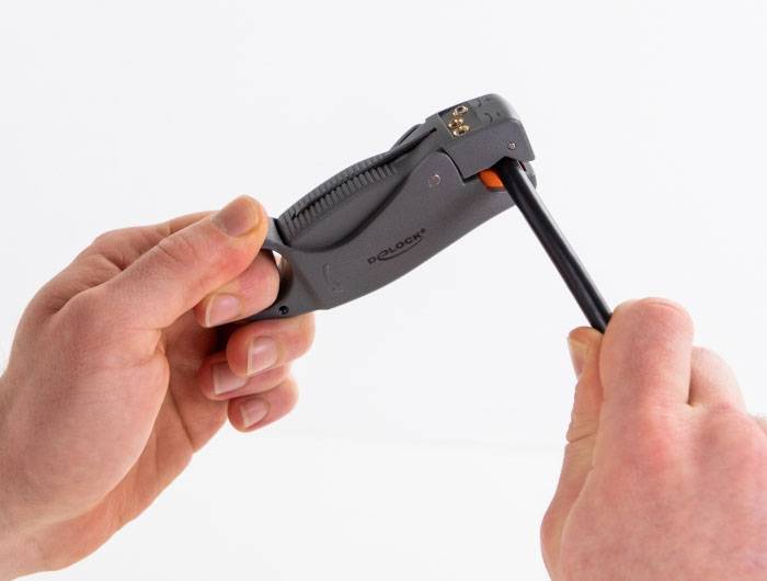 En hand håller ett kabelskalningsverktyg som skalpar en svart kabel. Verktyget avlägsnar isoleringen med precision.