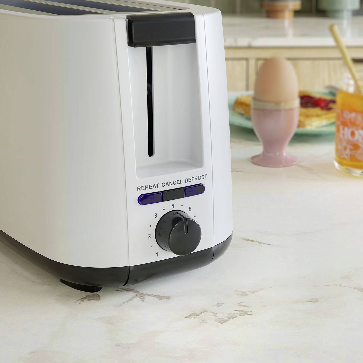 En brödrost står på en köksarbetsbänk. I bakgrunden syns ett löskokt ägg och ett glas juice.