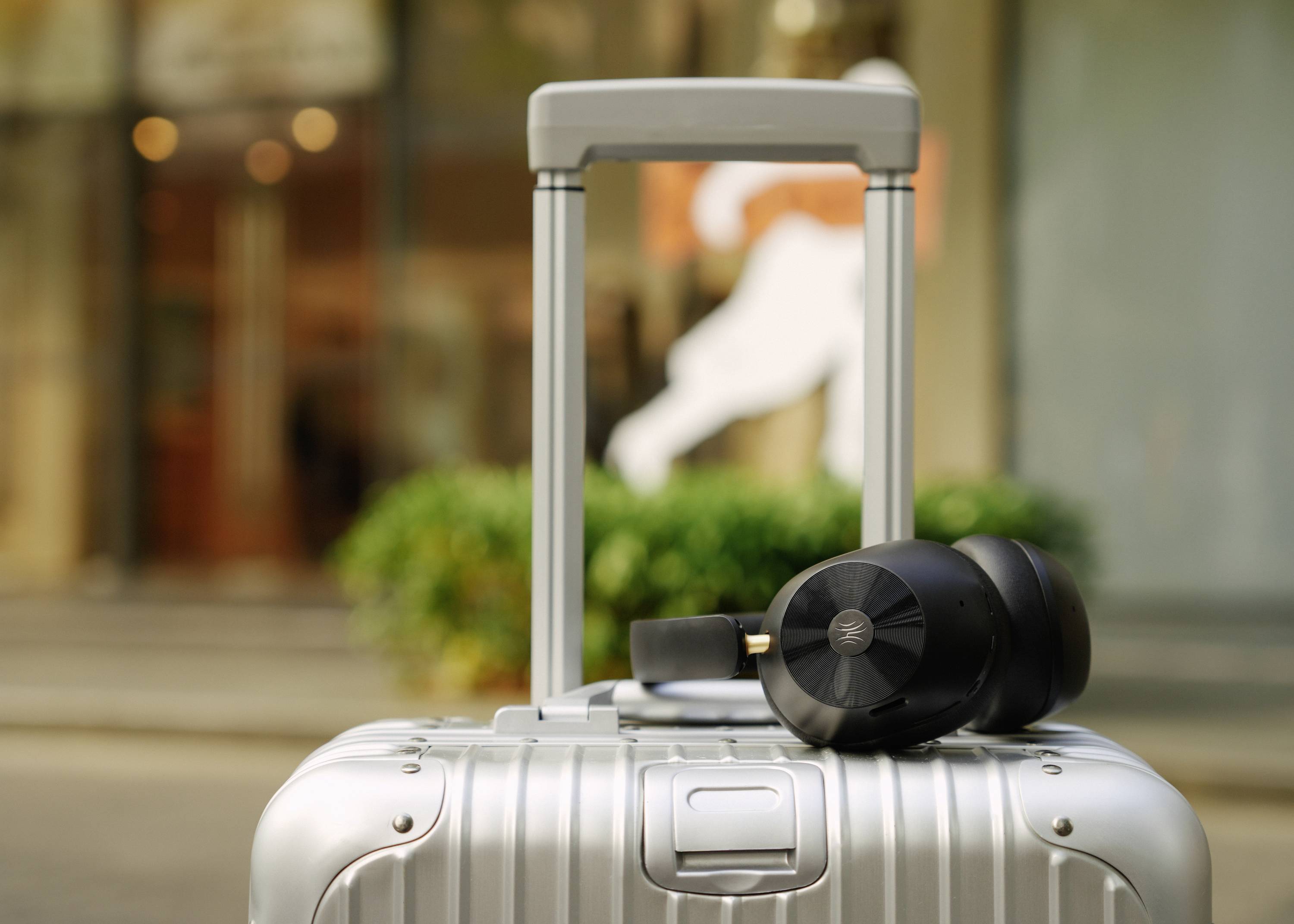 Silverfärgad resväska framför en skyltfönsterruta, där ett svart par hörlurar ligger. I bakgrunden syns en suddig förbipasserande.