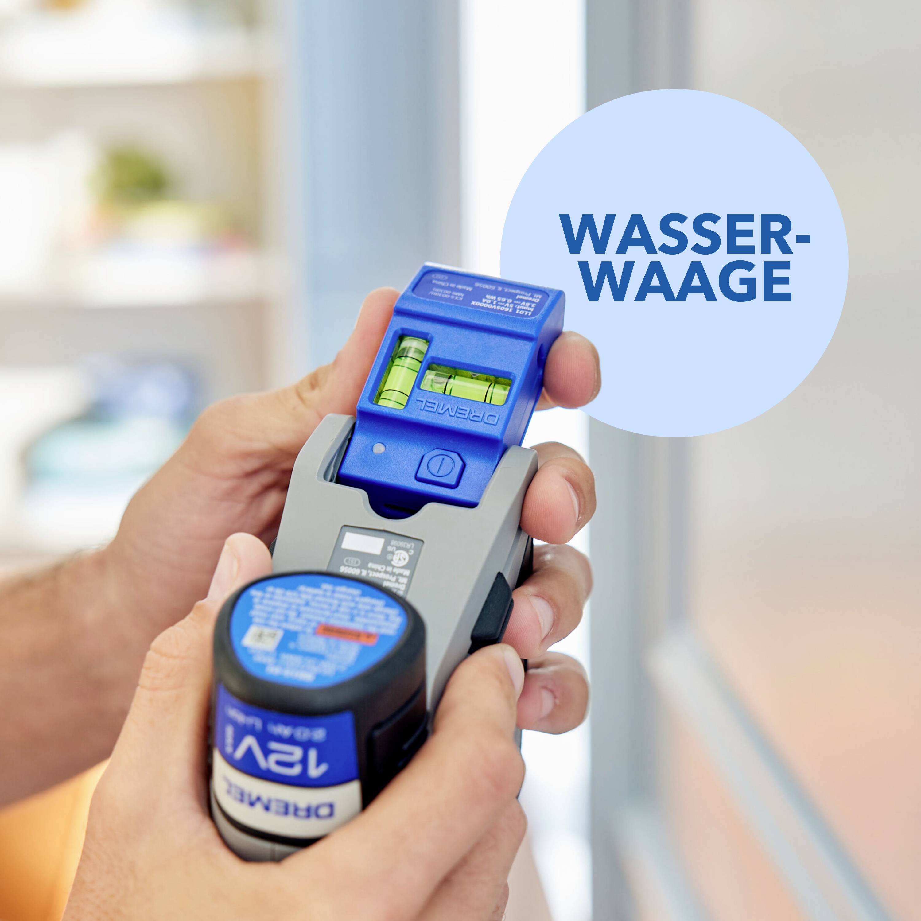 En person håller ett blå-grått mätinstrument med ett vattenpass. I bakgrunden syns ett suddigt fönster.