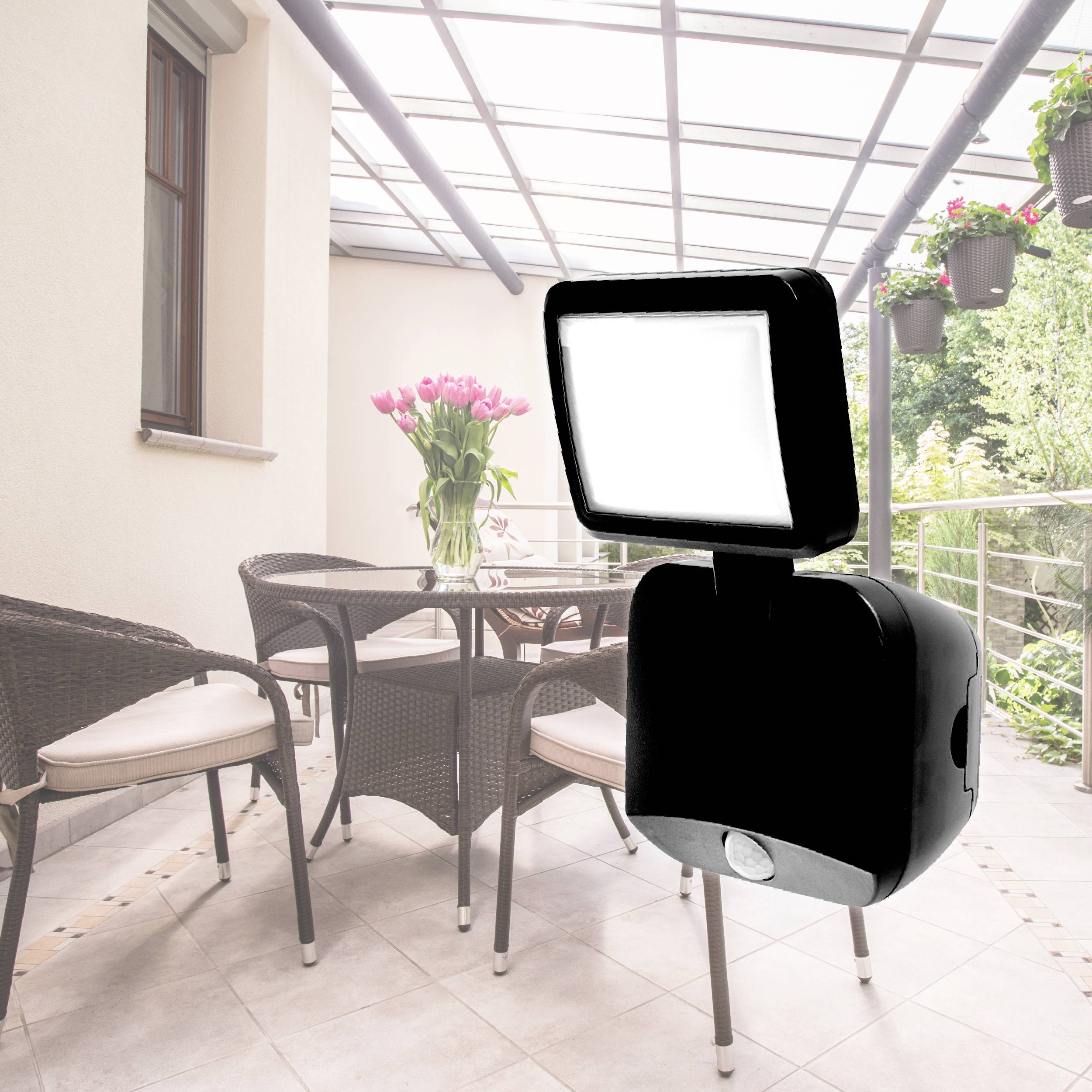 En modern LED-strålkastare belyser en terrass med rotatingmöbler och hängande blommor. Perfekt för utomhusbelysning under natten.