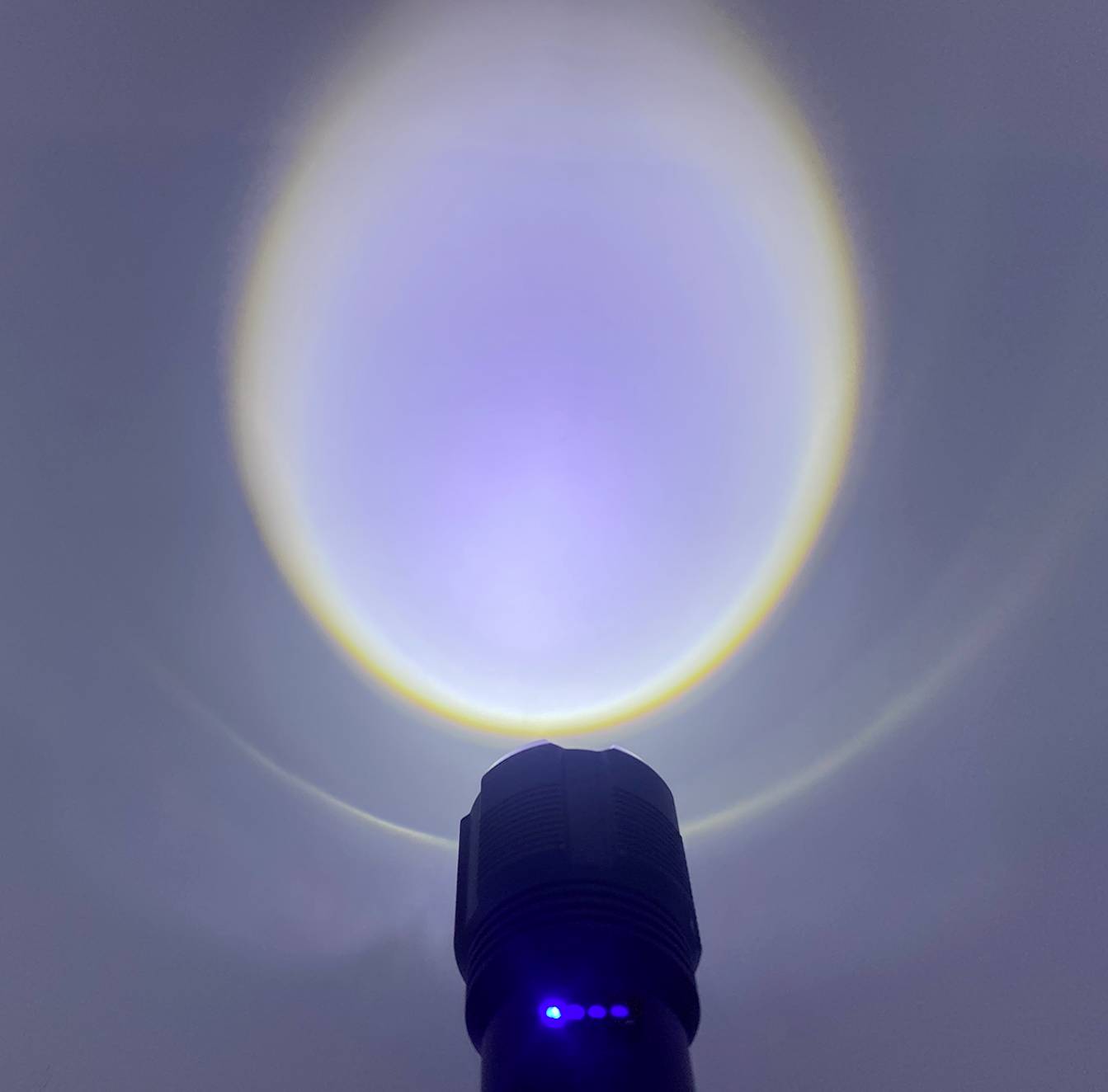 Ficklampa lyser mot en vägg och skapar en ljus ljuscirkel med blå och gul kant.