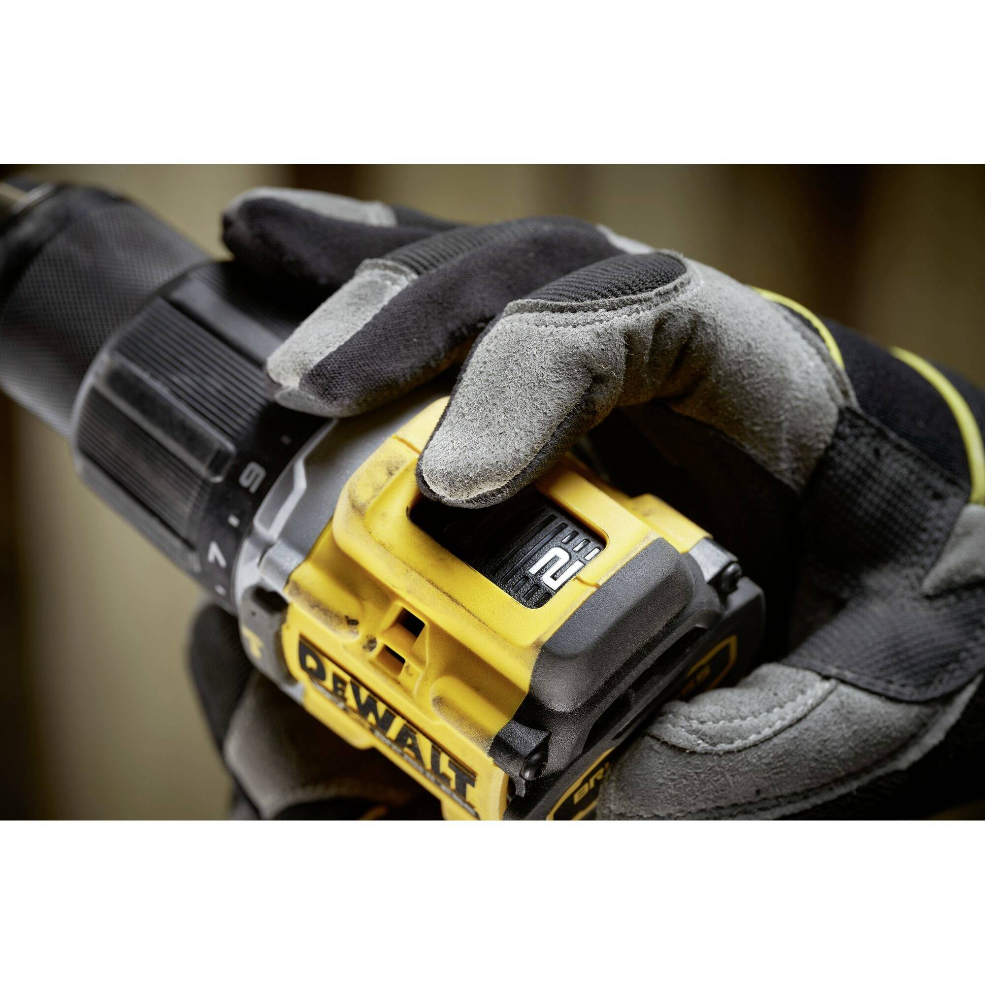 En person bär svarta och grå handskar och håller fast en elektrisk borr med ett gult DeWalt-märke.