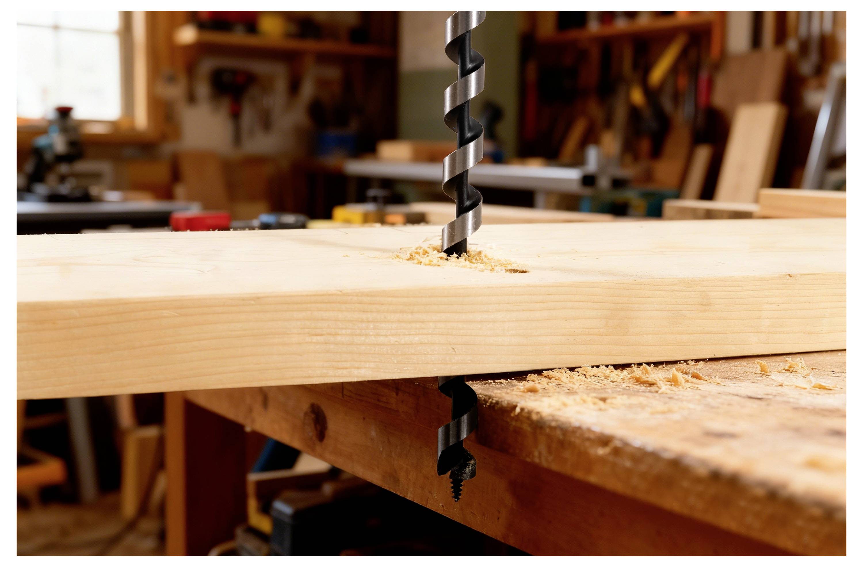 En borr tränger igenom en träplanka på en arbetsbank, med träspån utspridda runtomkring, och fångar ett ögonblick inom träbearbetning.