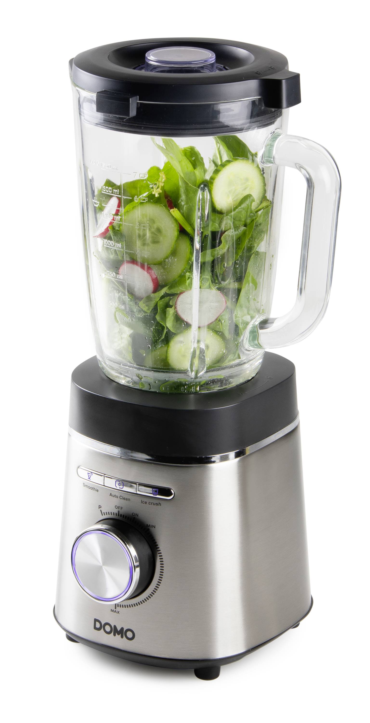 Mixer med glaskanna, fylld med gurkskivor, spenat och rädisor. Apparat av metall med manövreringsknapp och varumärkelogotyp 'DOMO'.