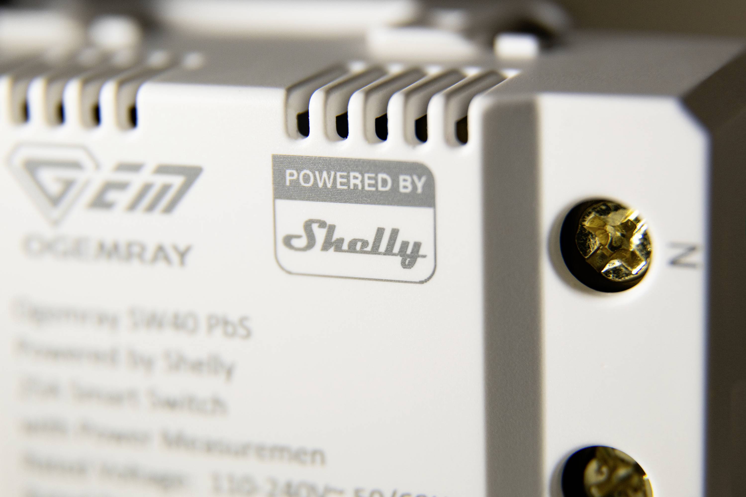 Närbild av en enhet märkt 'POWERED BY Shelly', visar tekniska detaljer hos en elektronisk switch.