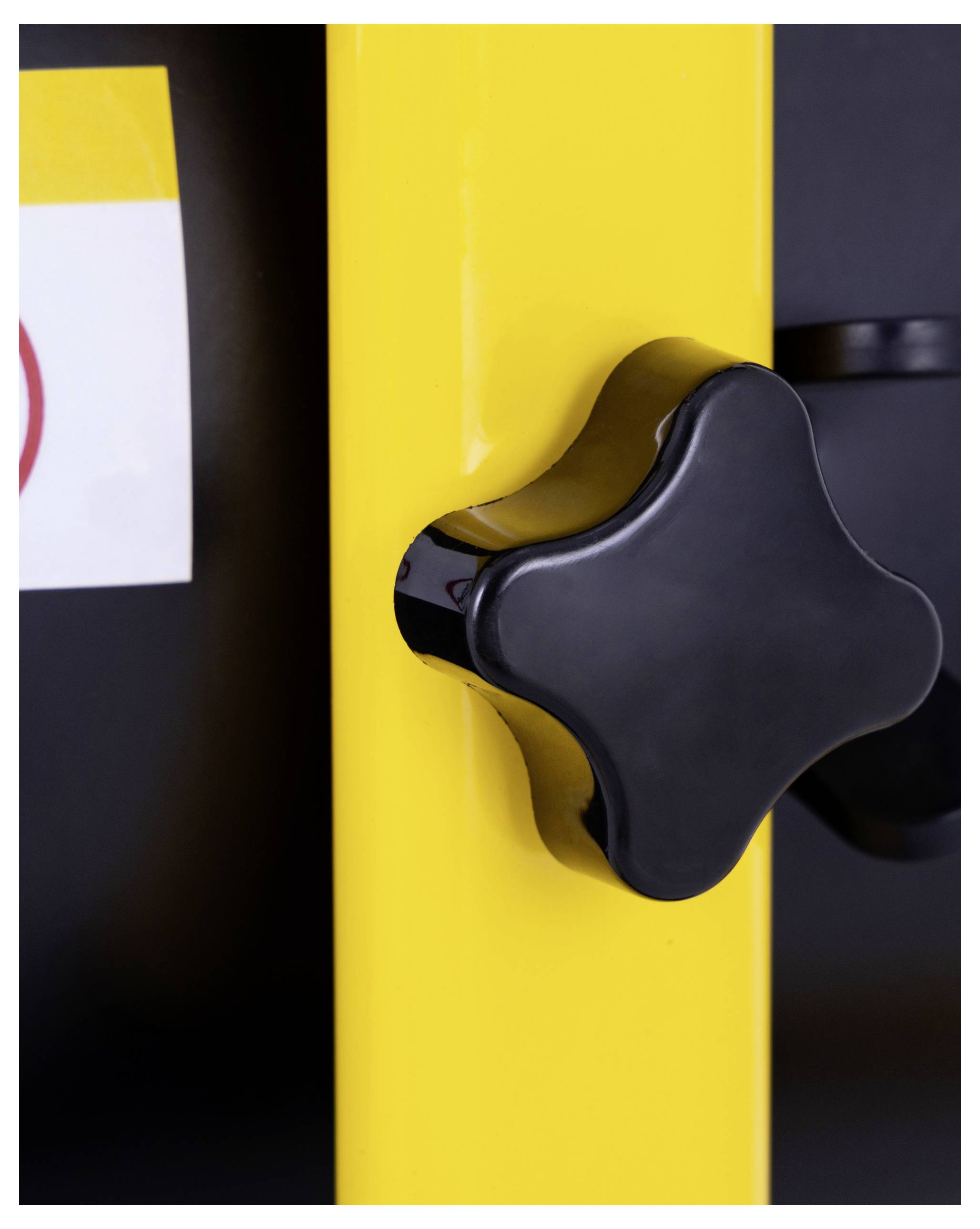 En närbild av ett svart stjärnformat handtag på en gul metallyta, sannolikt en del av en maskin eller utrustning.