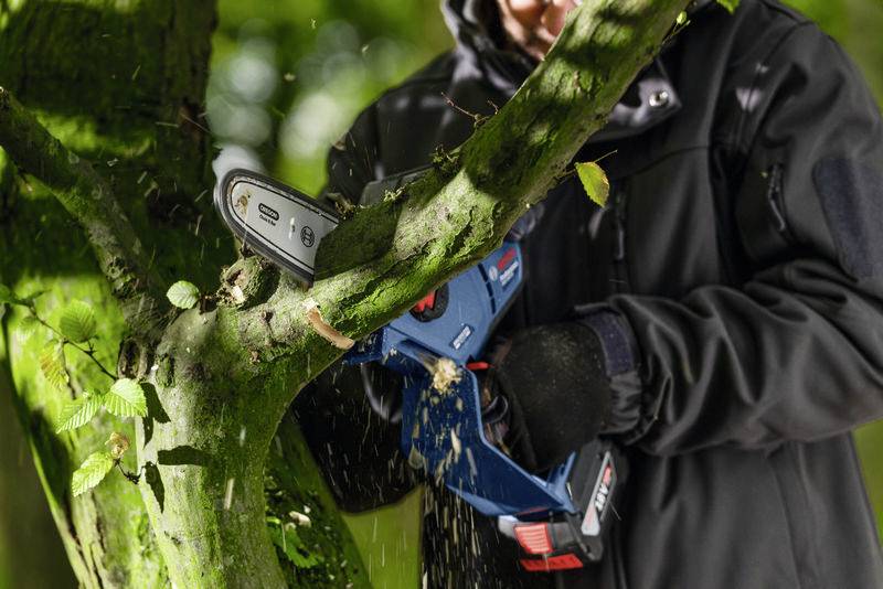 En person sågar av en gren med en praktisk elsåg i skogen.