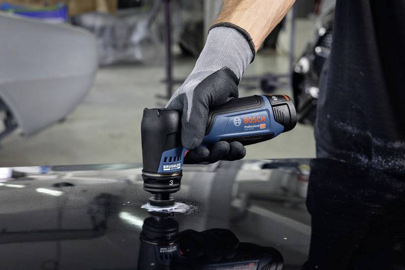En person använder en Bosch handhållen polermaskin på en svart yta; enheten styrs med en handskklädd hand.