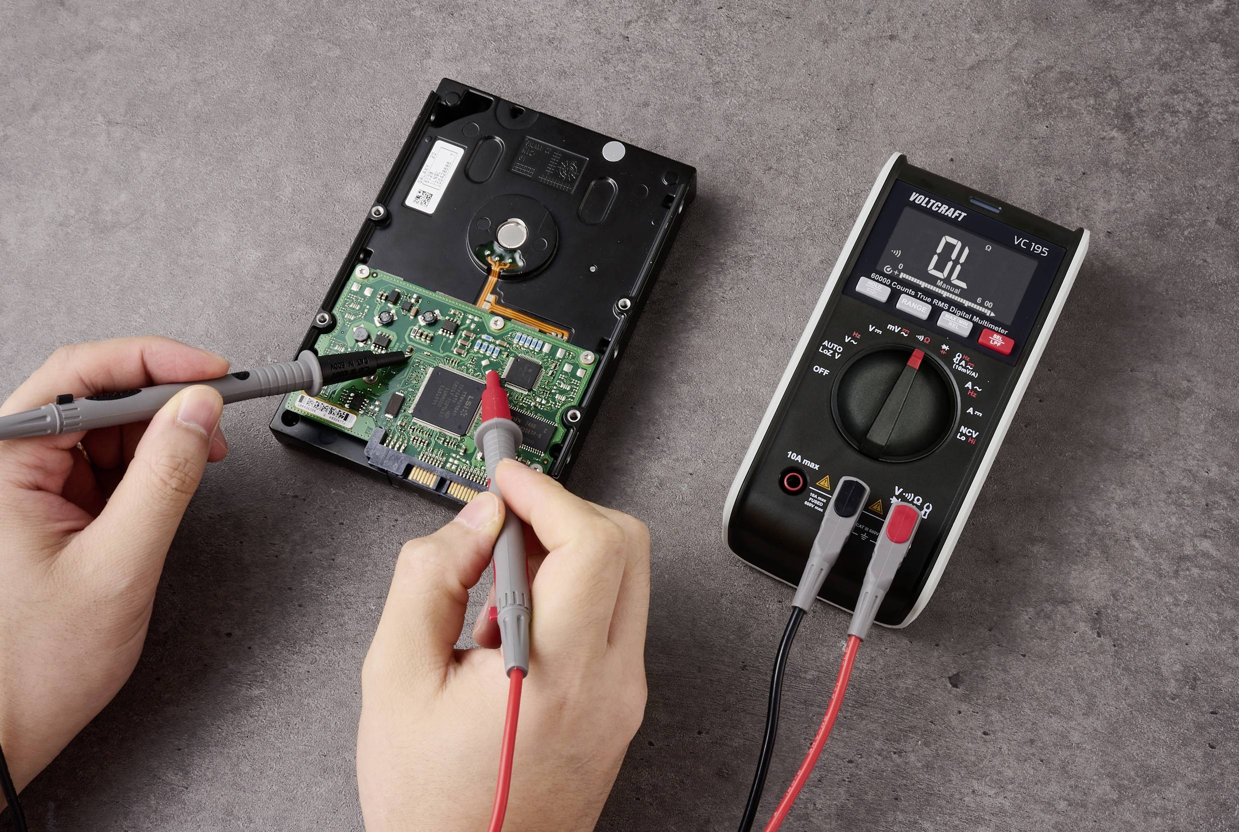 En person använder en multimeter för att testa en öppen hårddisk och mäter elektriska värden på kretskortet.