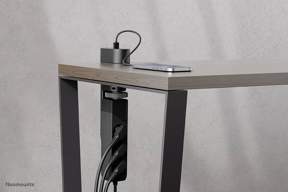 Ett bord med en kabelhanterare under, där flera kablar är anslutna; på bordet ligger en laddare och en smarttelefon.