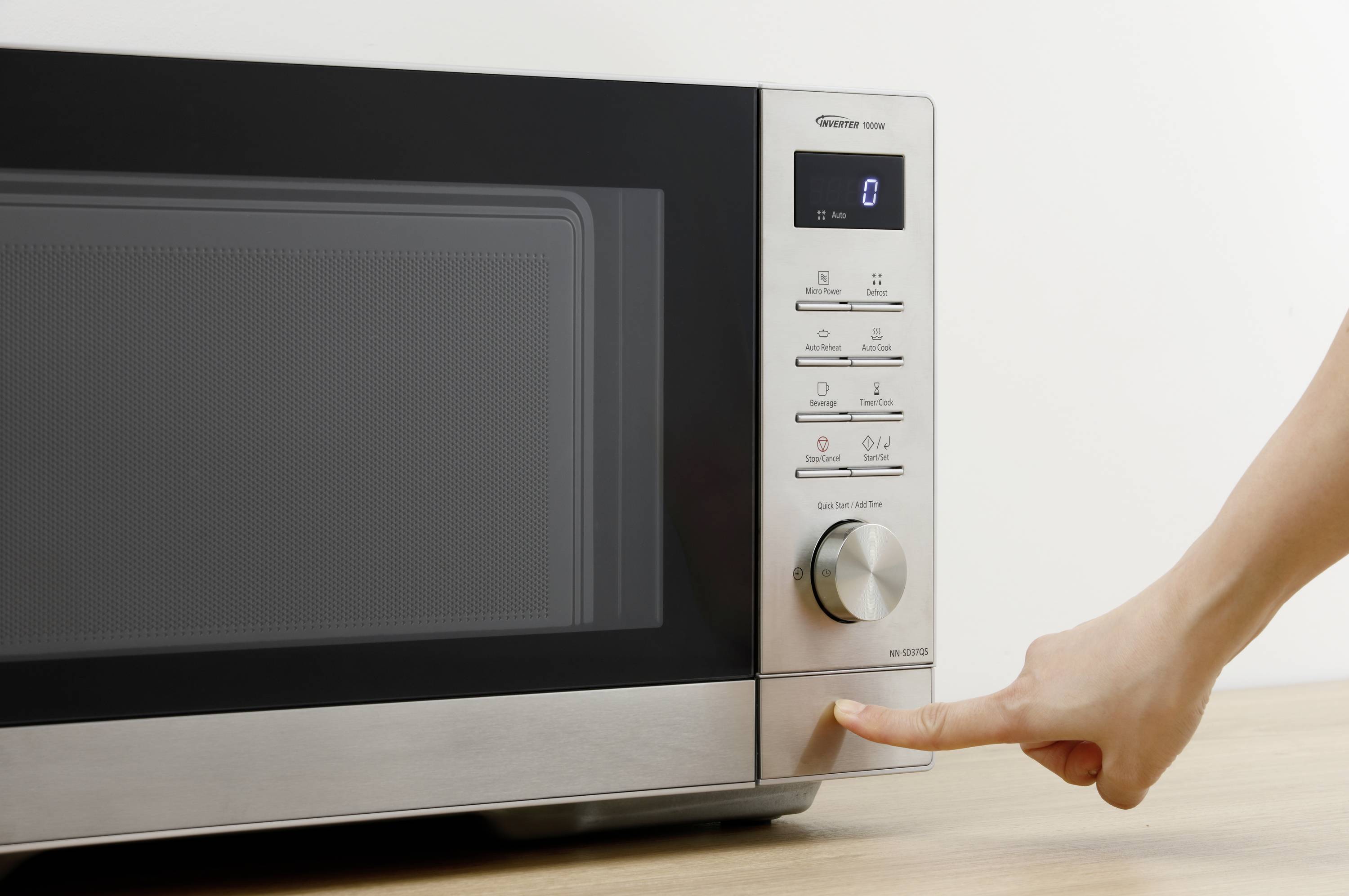 En person trycker på knappen på en modern mikrovågsugn med digitalt displej och olika inställningsalternativ.
