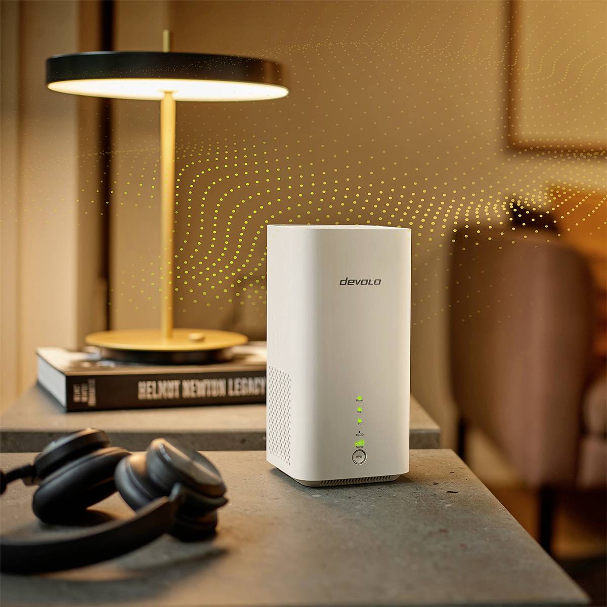 En vit WiFi-router står på ett bord bredvid en lampskärm, några böcker och ett par hörlurar.