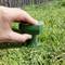En hand placerar en grön gräsSpridare på en grön gräsmatta. Trästaket i bakgrunden.