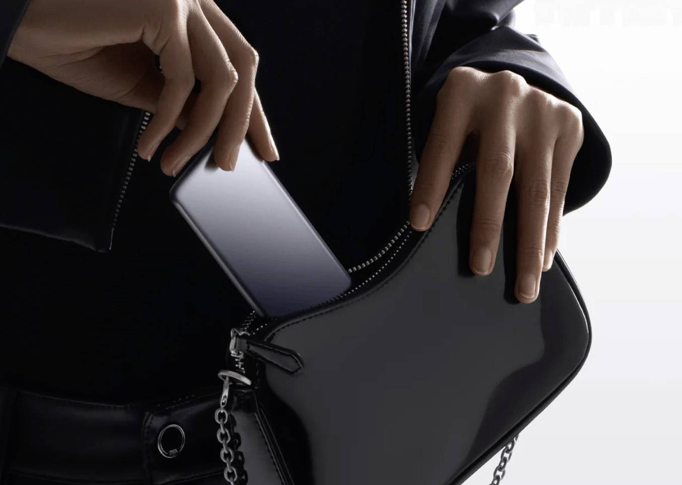 En person lägger en smartphone i en svart handväska, vilket framhäver telefonens eleganta design och bärbarhet.