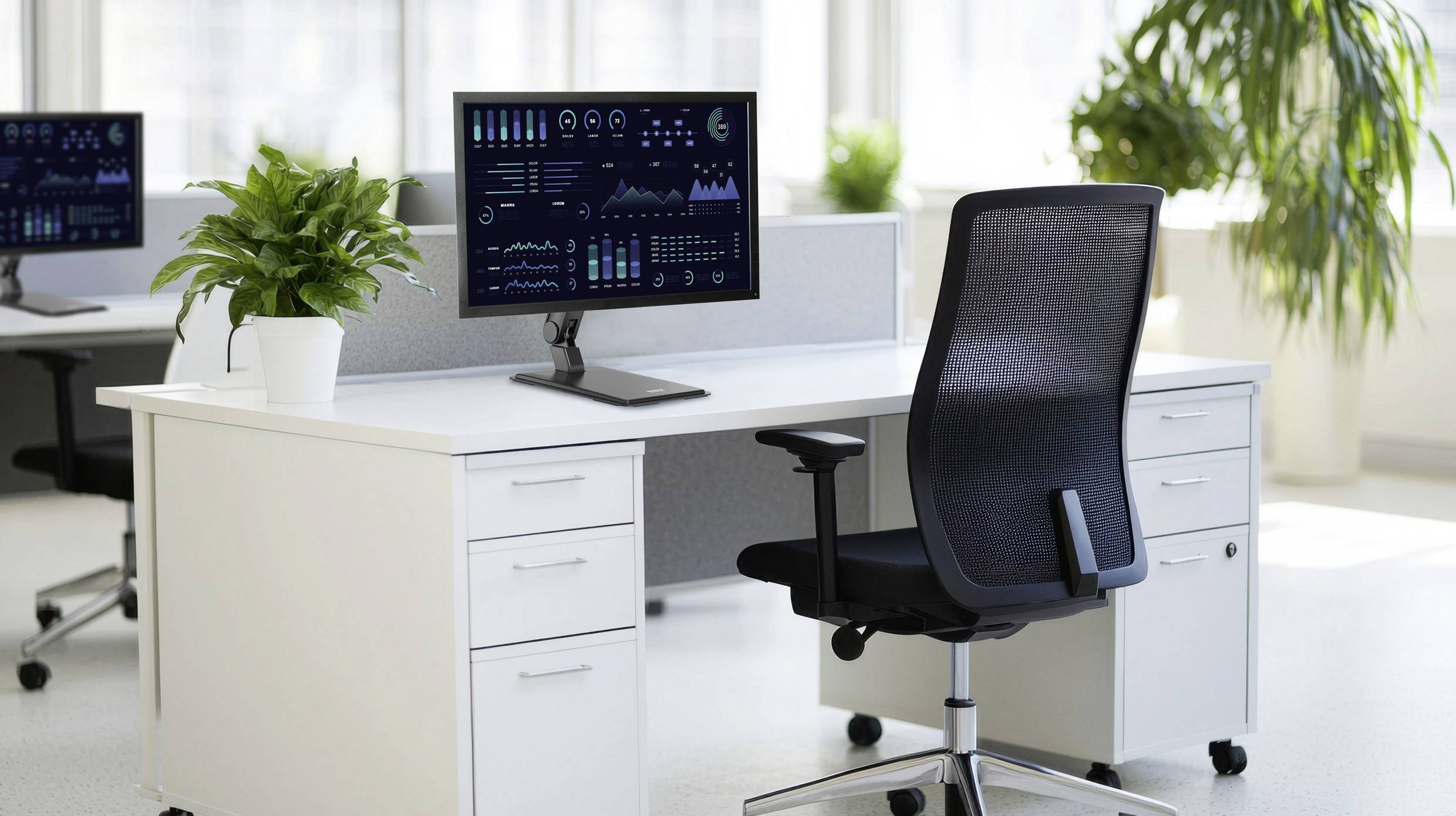 Modernt kontor med två skrivbord, vart och ett utrustat med en dator som visar resultatgrafer. En kontorsstol och krukväxter kompletterar inredningen.