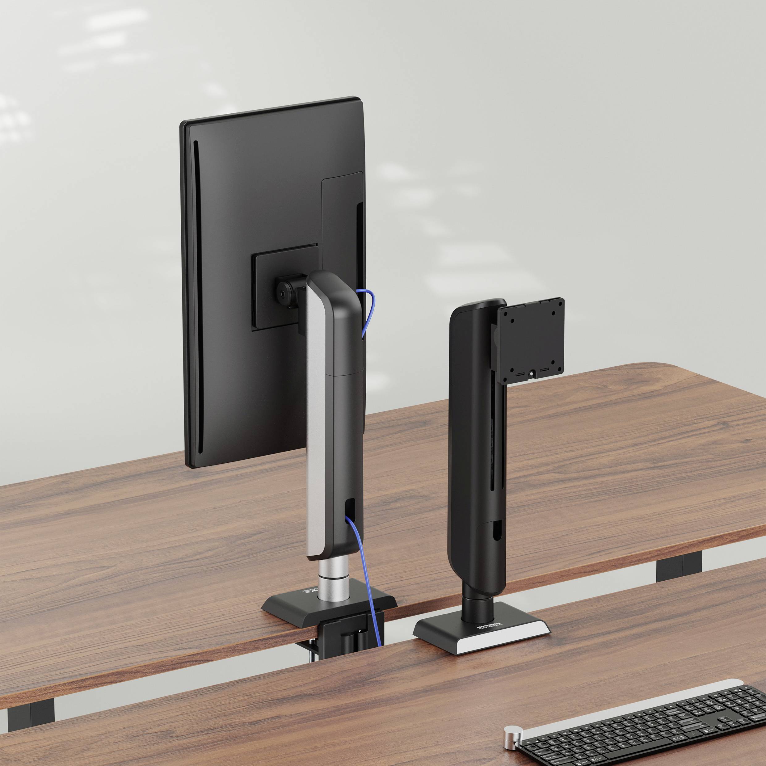 Två datorskärmar med bordsstativ är placerade sida vid sida på ett träskrivbord, sedda bakifrån.