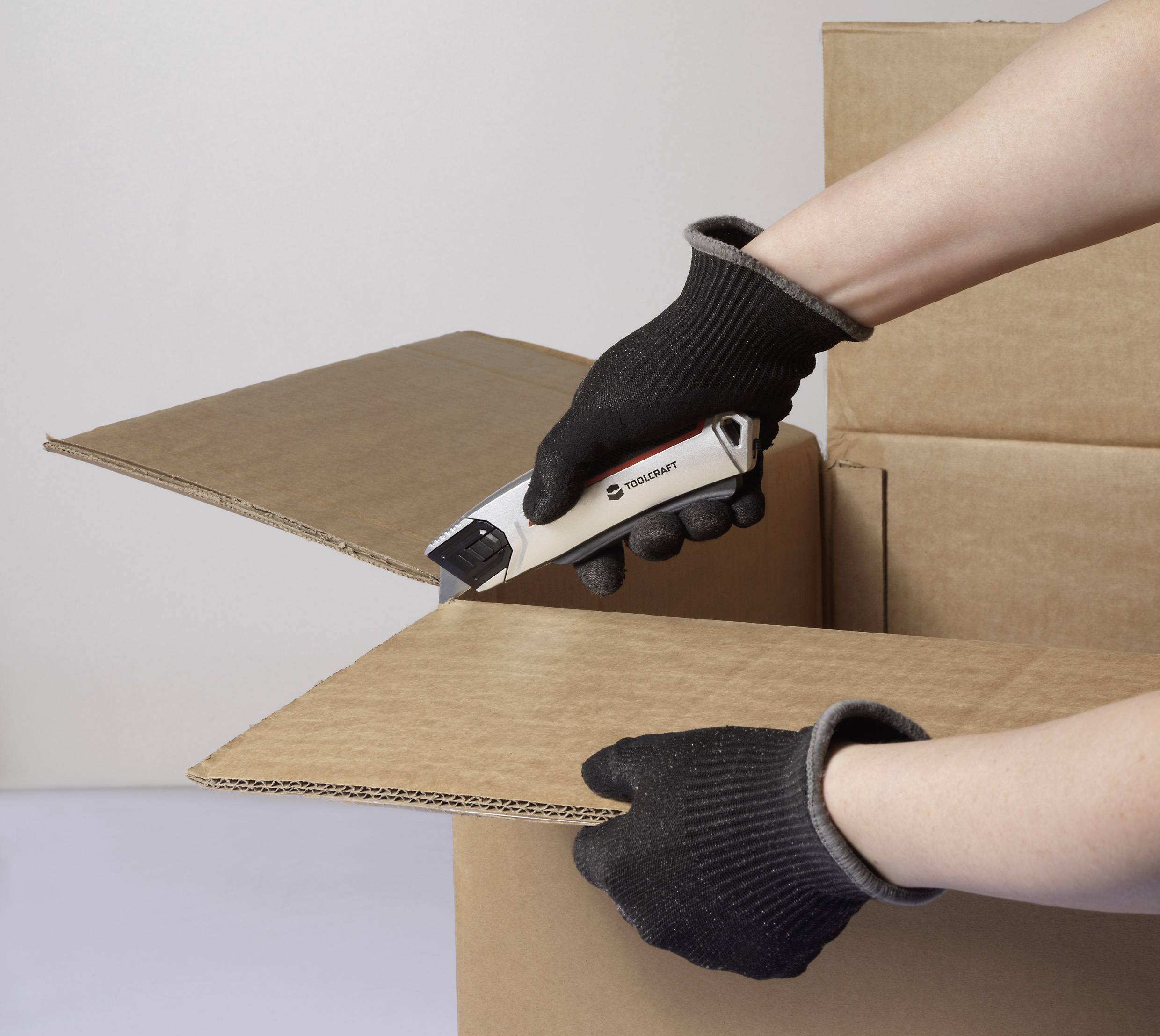 En person som bär handskar använder en säker boxkniv för att försiktigt öppna en kartong.